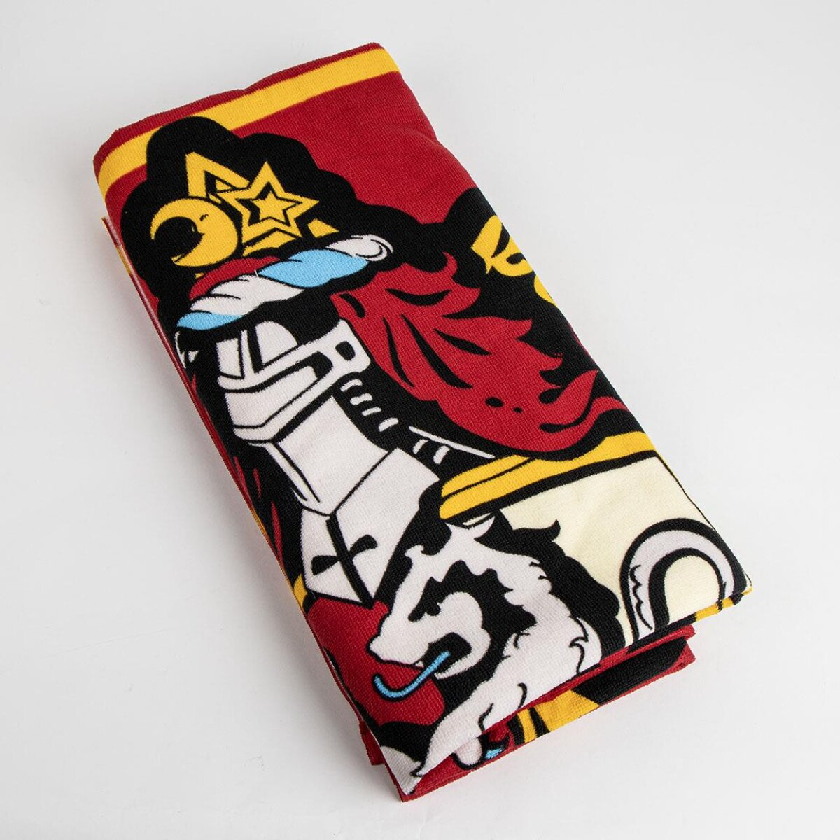 Toalla roja doblada con diseño de caballero, estrella y león. El fondo es blanco. La toalla tiene detalles amarillos y negros.