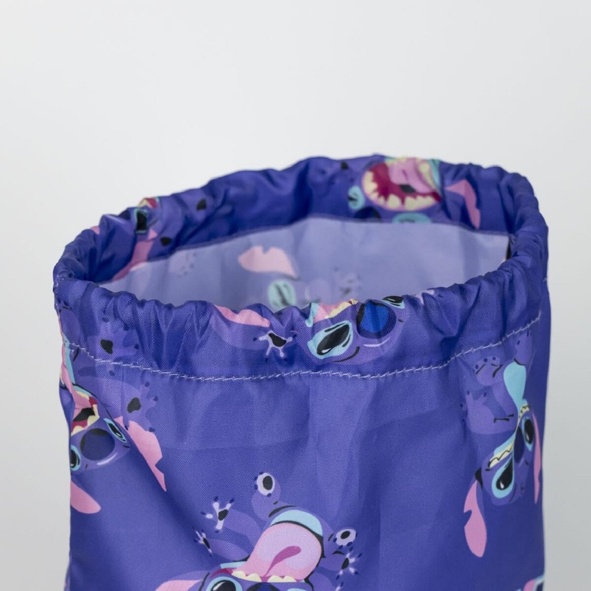 Una bolsa morada con cordón con un estampado de la cara de un personaje de dibujos animados se muestra sobre un fondo blanco, la bolsa está abierta.
