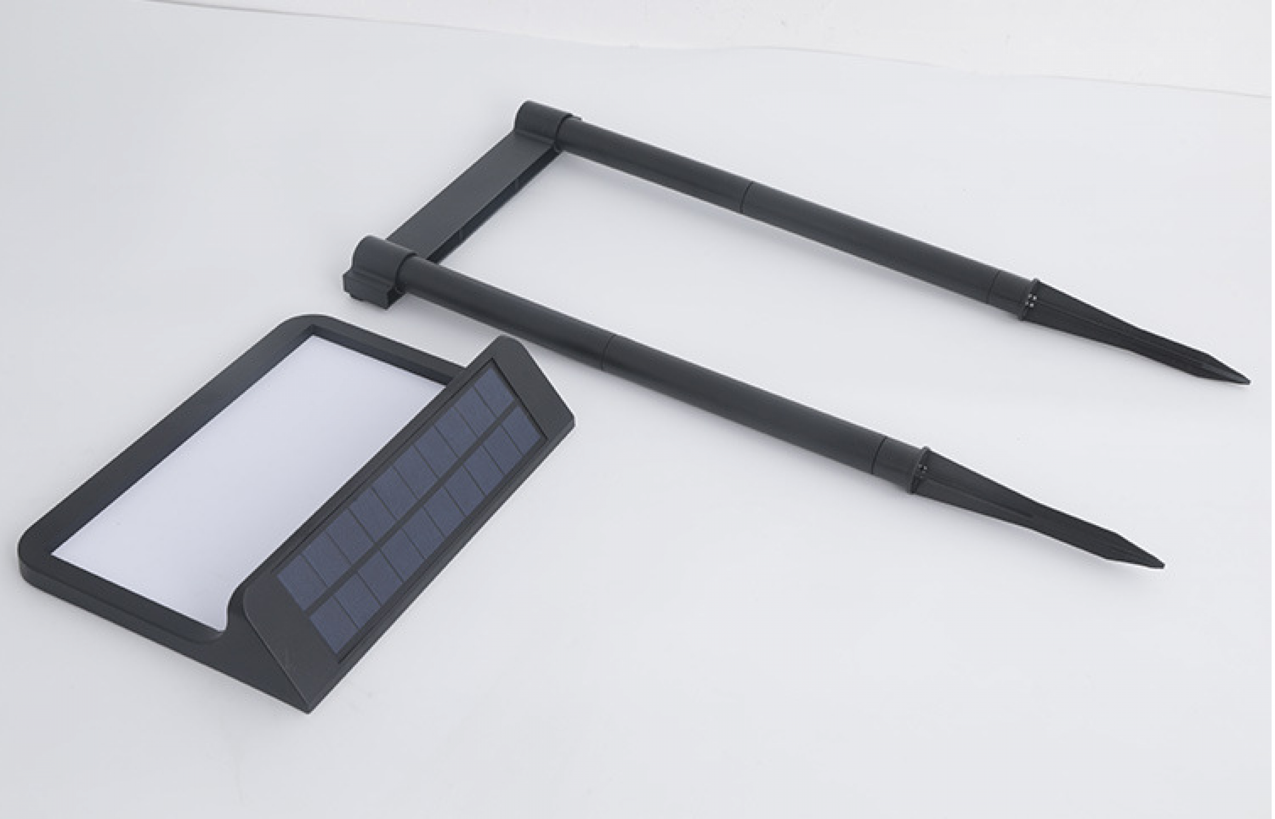 Schwarze Solar-Gartenlichtkomponenten. Eines mit Solarpanel, ein anderes mit zwei Pfählen. Alles auf weißer Oberfläche.