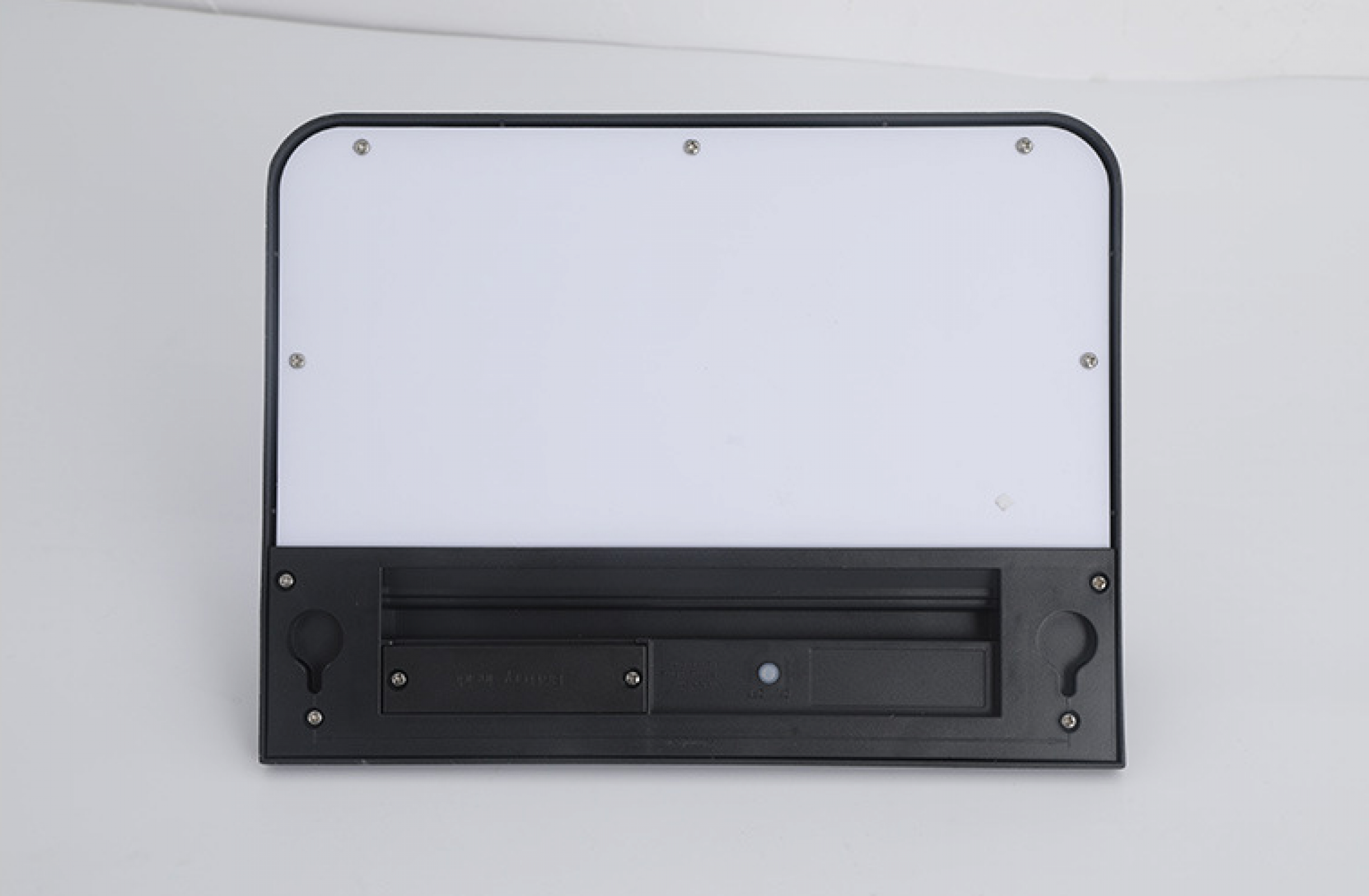 Eine schwarze, rechteckige LED-Leuchte mit weißem Lichtpaneel auf weißem Hintergrund. Schrauben befestigen das Paneel.