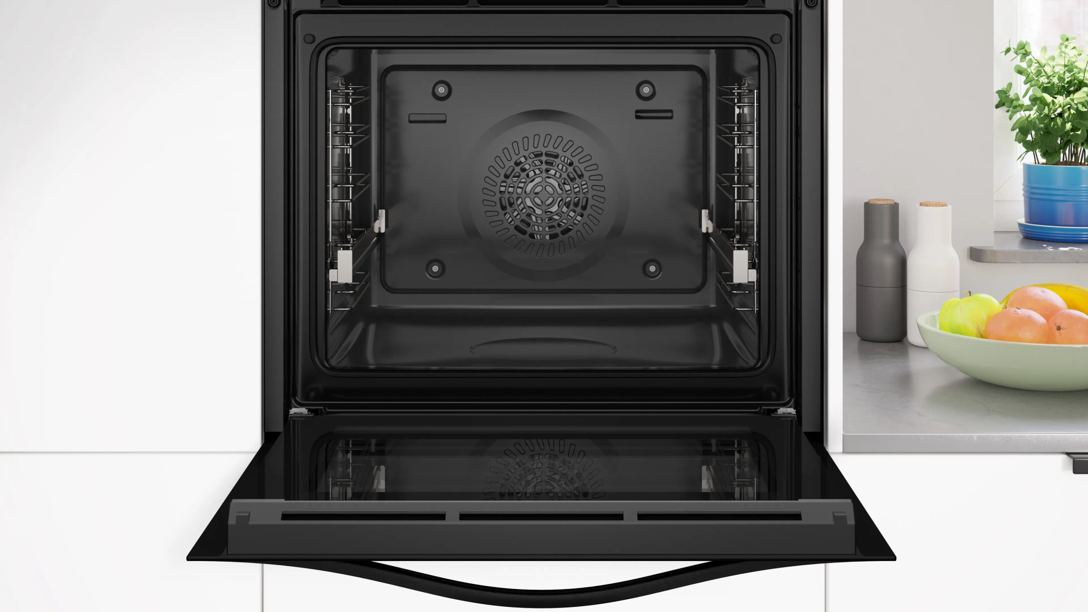 Forno aperto con interno nero, porta aperta e una scena di cucina con frutta e piante sullo sfondo.