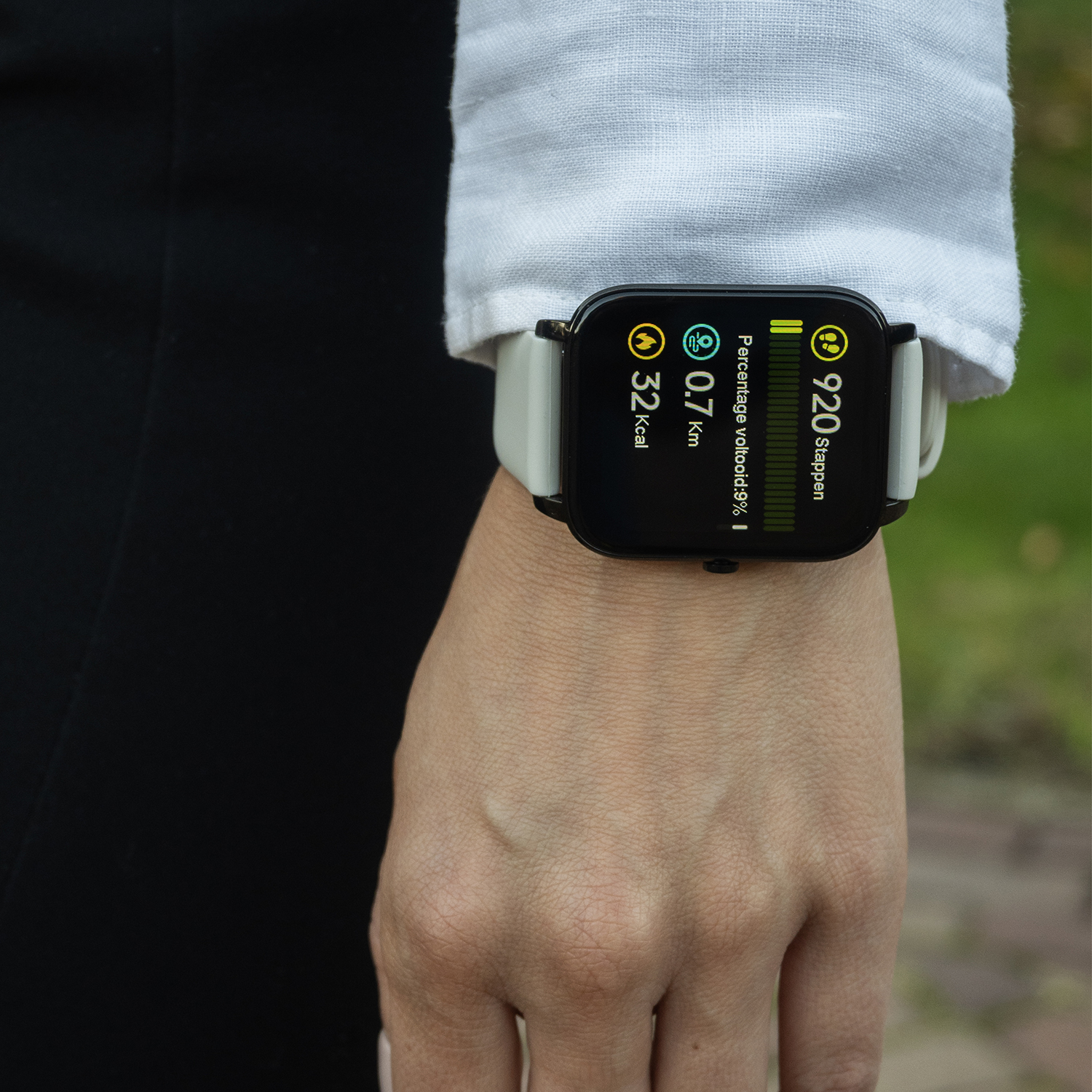 De pols van een persoon met een smartwatch die statistieken weergeeft: stappen, afstand, calorieën en percentage. De persoon draagt een wit overhemd.