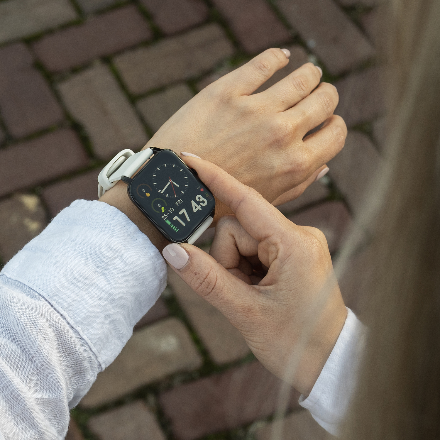 Een persoon die een smartwatch buiten draagt. Het horloge geeft de tijd weer. De achtergrond is een bakstenen voetpad.