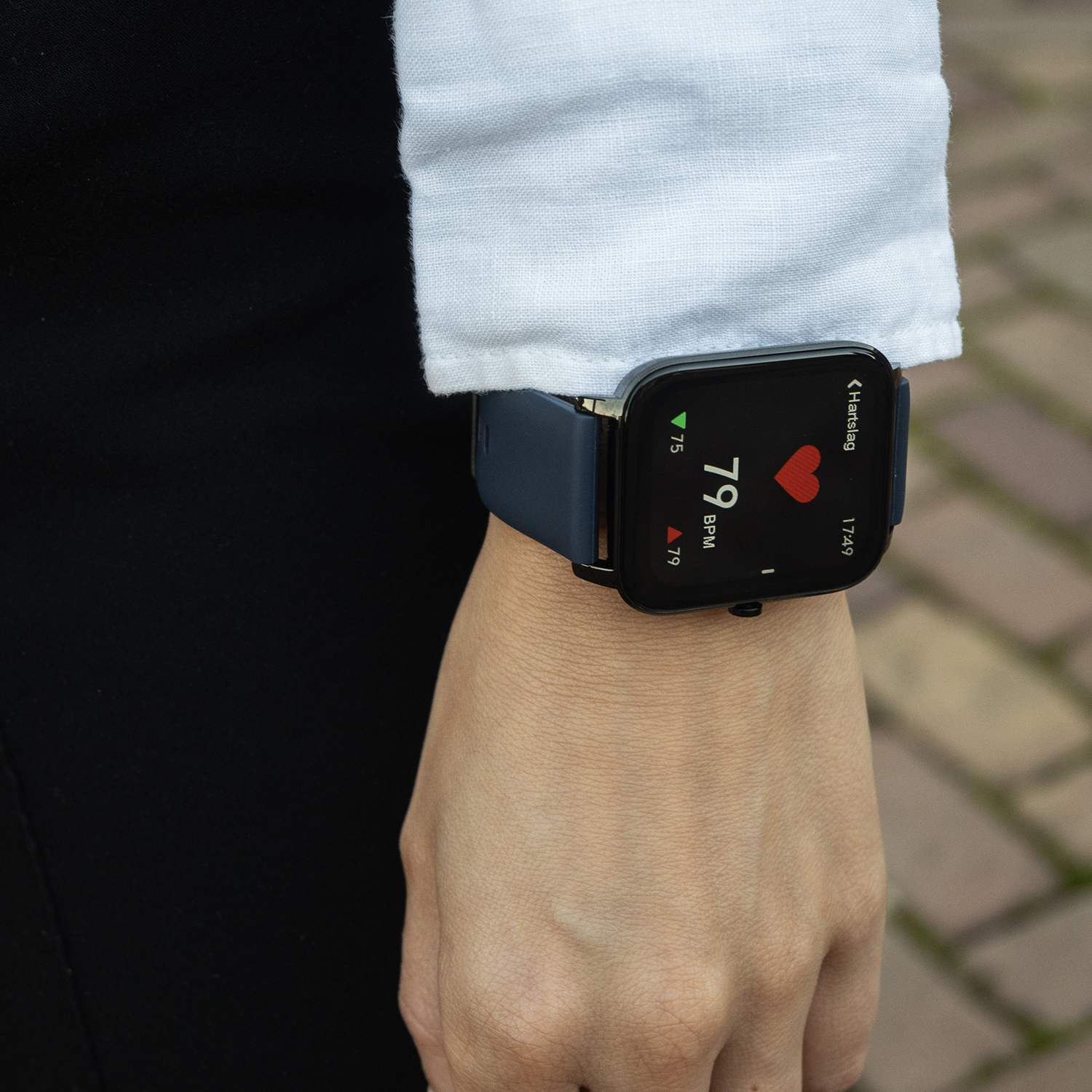 Pols van een persoon met een blauwe smartwatch die een hartslag van 79 BPM weergeeft. Het horloge zit om een lichte huidhand, en de achtergrond is wazig.