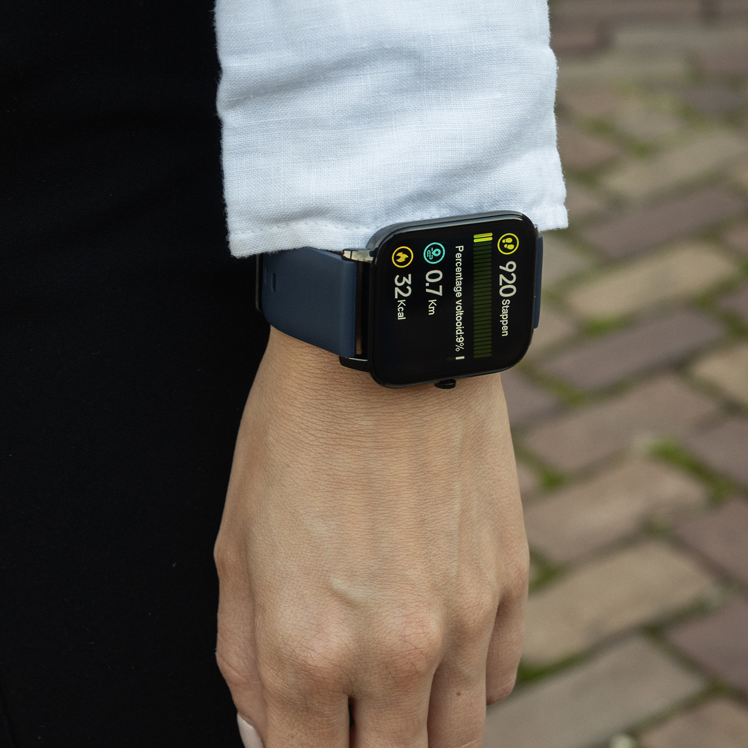 Een pols met een smartwatch die stappen, afstand en calorieën weergeeft. De persoon draagt een wit overhemd en zwarte kleding.