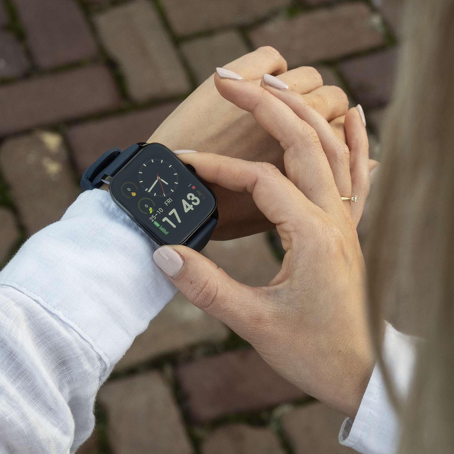 Een persoon met een smartwatch controleert de tijd, met datum en tijd weergegeven. De persoon is buiten en de achtergrond is wazig.