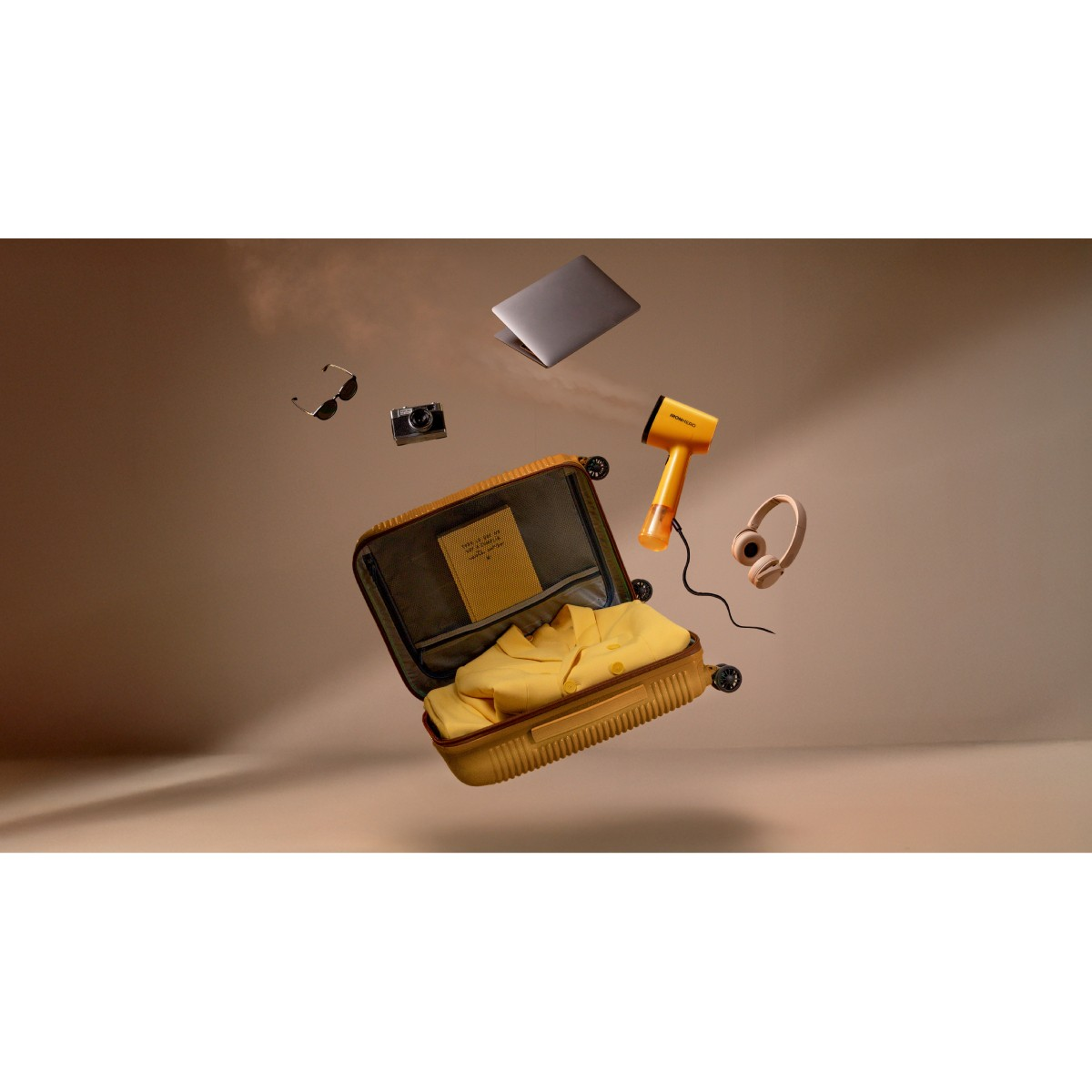 A yellow suitcase is open with a yellow shirt inside. Other items floating in the air are a laptop, headphones, camera, and hair dryer.