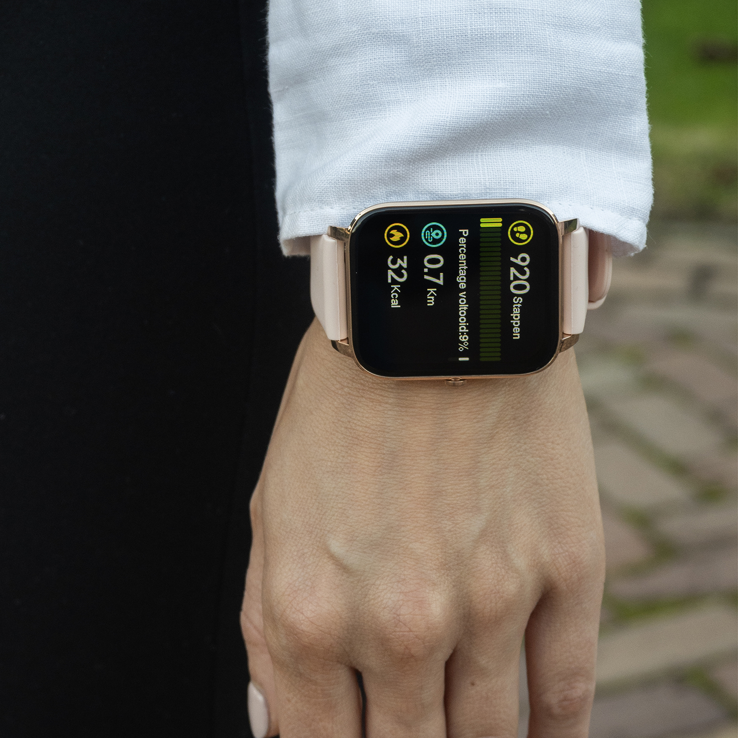 Een persoon die een smartwatch draagt die stappen, afstand en calorieën weergeeft. Het horloge zit om een pols met een wit overhemd en zwarte kleding.