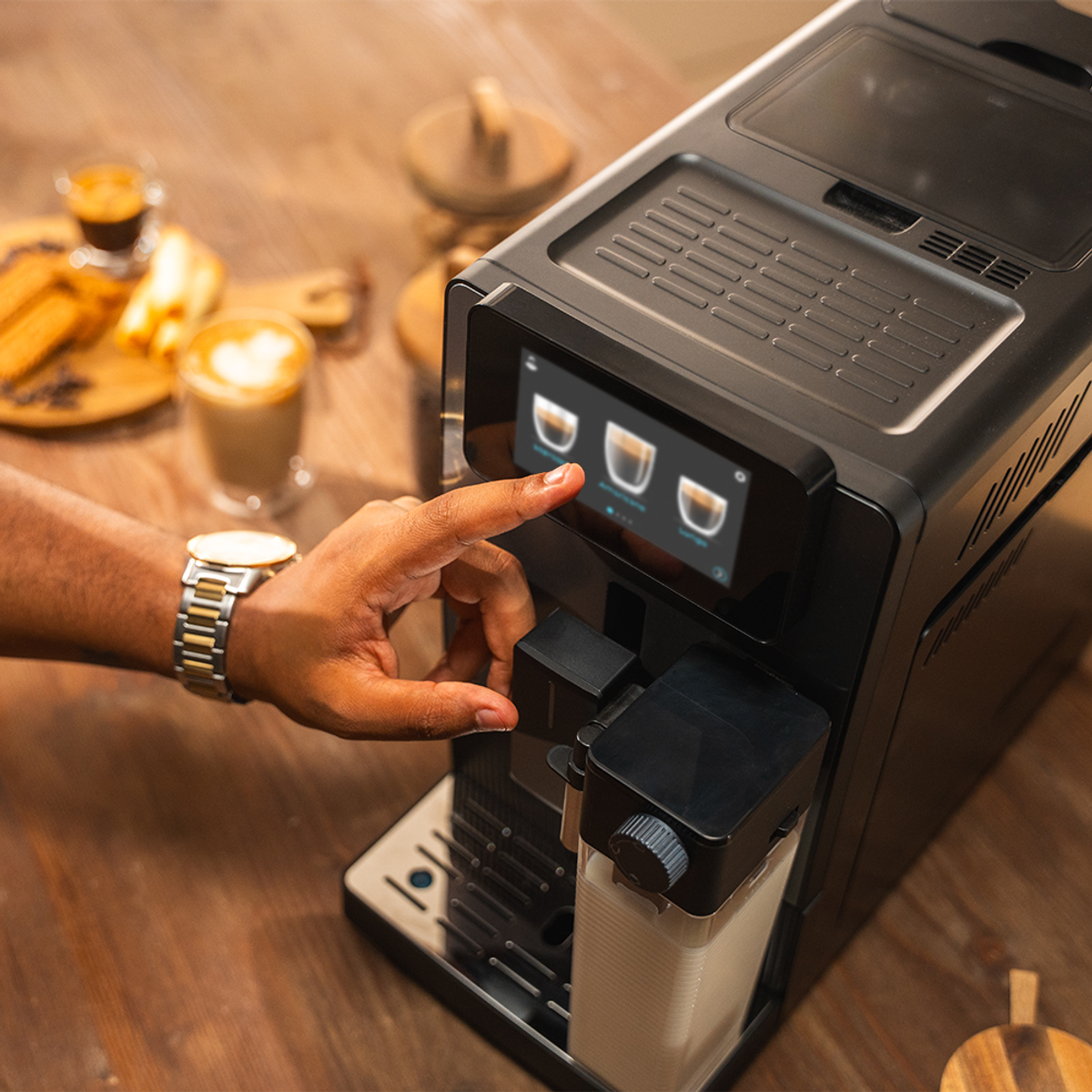 Un dito tocca lo schermo di una macchina da caffè. Vengono visualizzate le opzioni espresso. Lo sfondo include tazze da caffè ed elementi in legno.