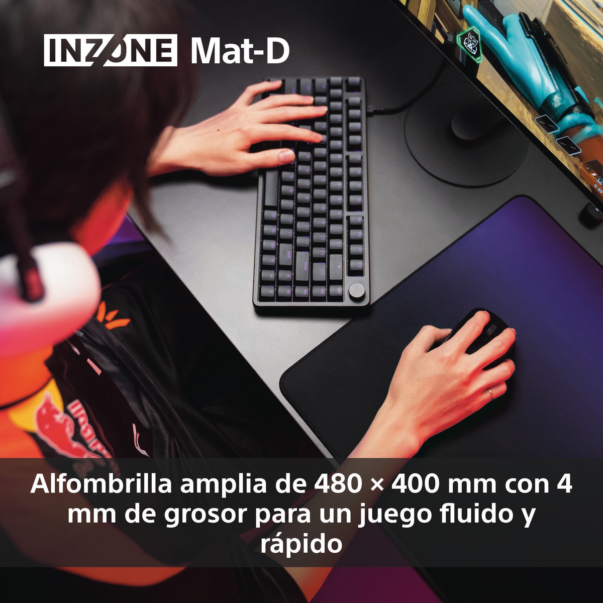 Les mains d'une personne sur un clavier et un tapis de souris. Un écran affiche un jeu. Le clavier et le tapis sont sur un bureau.