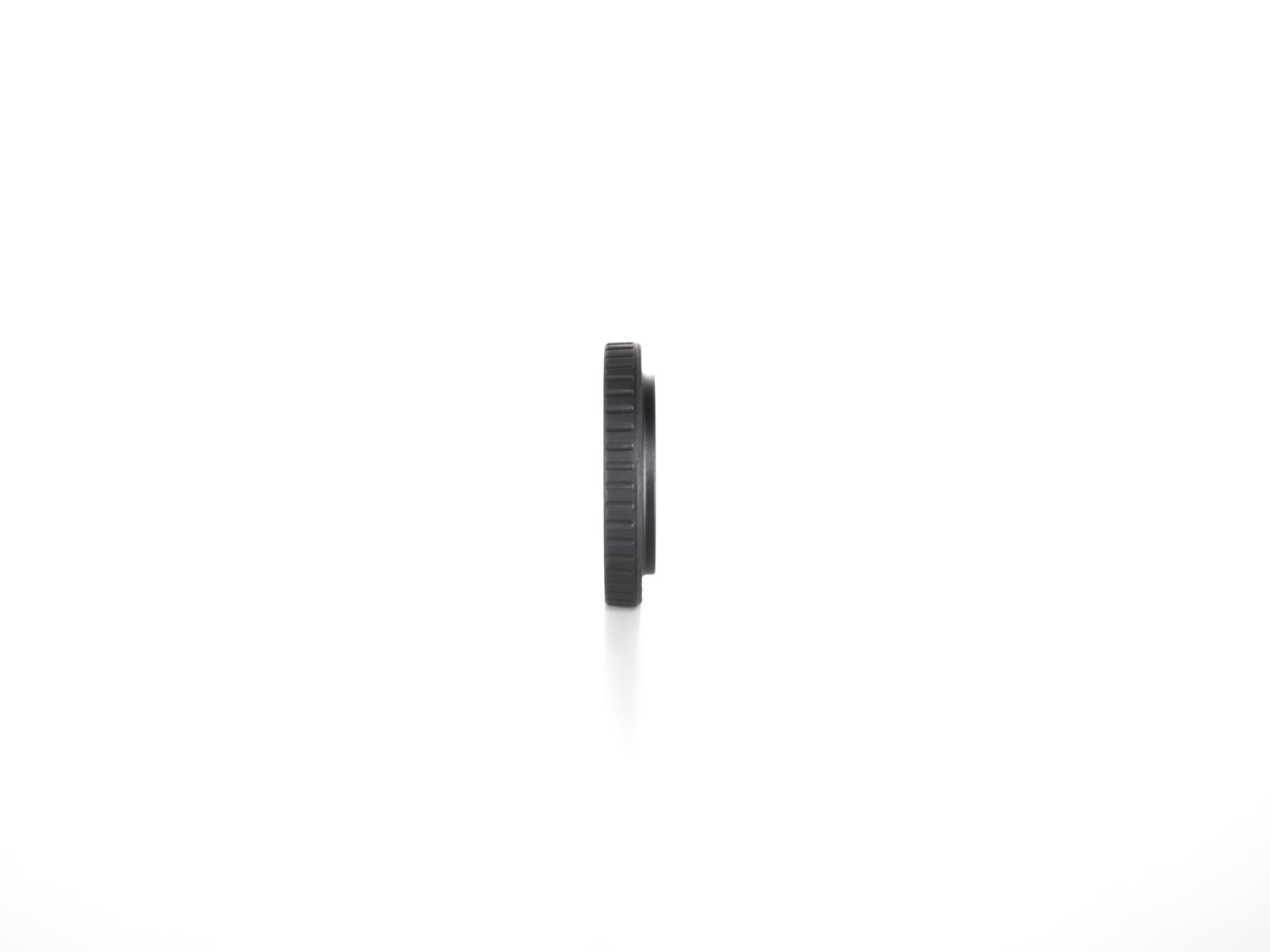 Un adaptador de lente negro está verticalmente contra un fondo blanco. Es cilíndrico con crestas en su borde exterior.