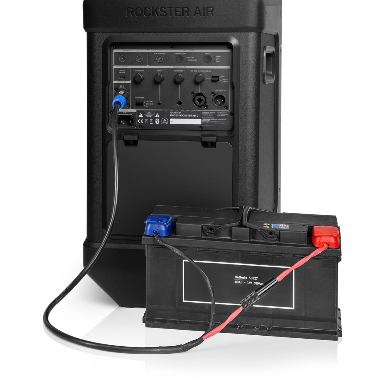 Ein schwarzer Lautsprecher, der mit einer Autobatterie mit roten und blauen Anschlüssen verbunden ist. Weißer Hintergrund. Der Lautsprecher sagt ROCKSTER AIR.