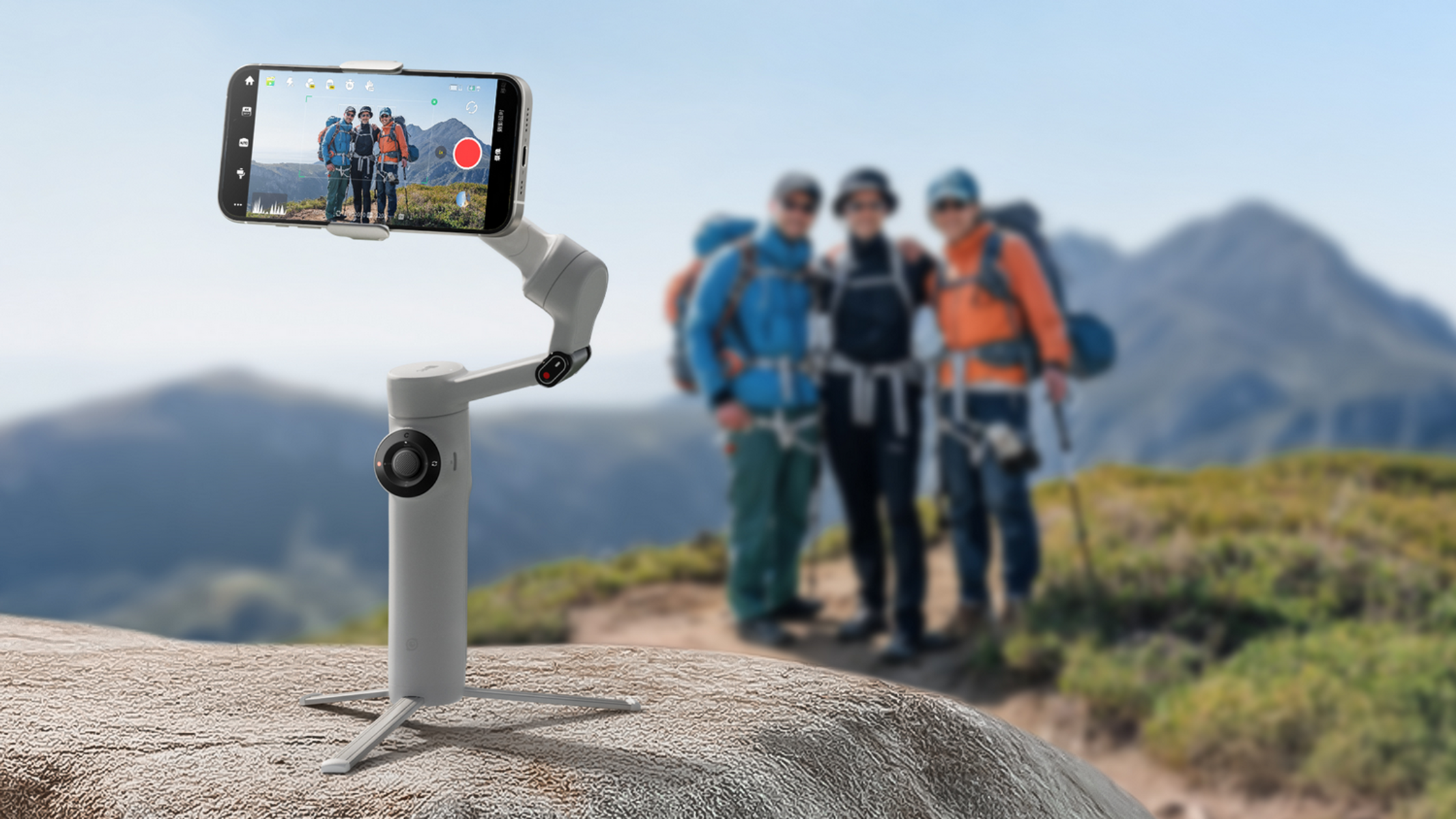 Ein Telefon zeichnet Wanderer auf einem Berg auf. Ein Gimbal hält das Telefon. Der Hintergrund zeigt Wanderer und Berge.