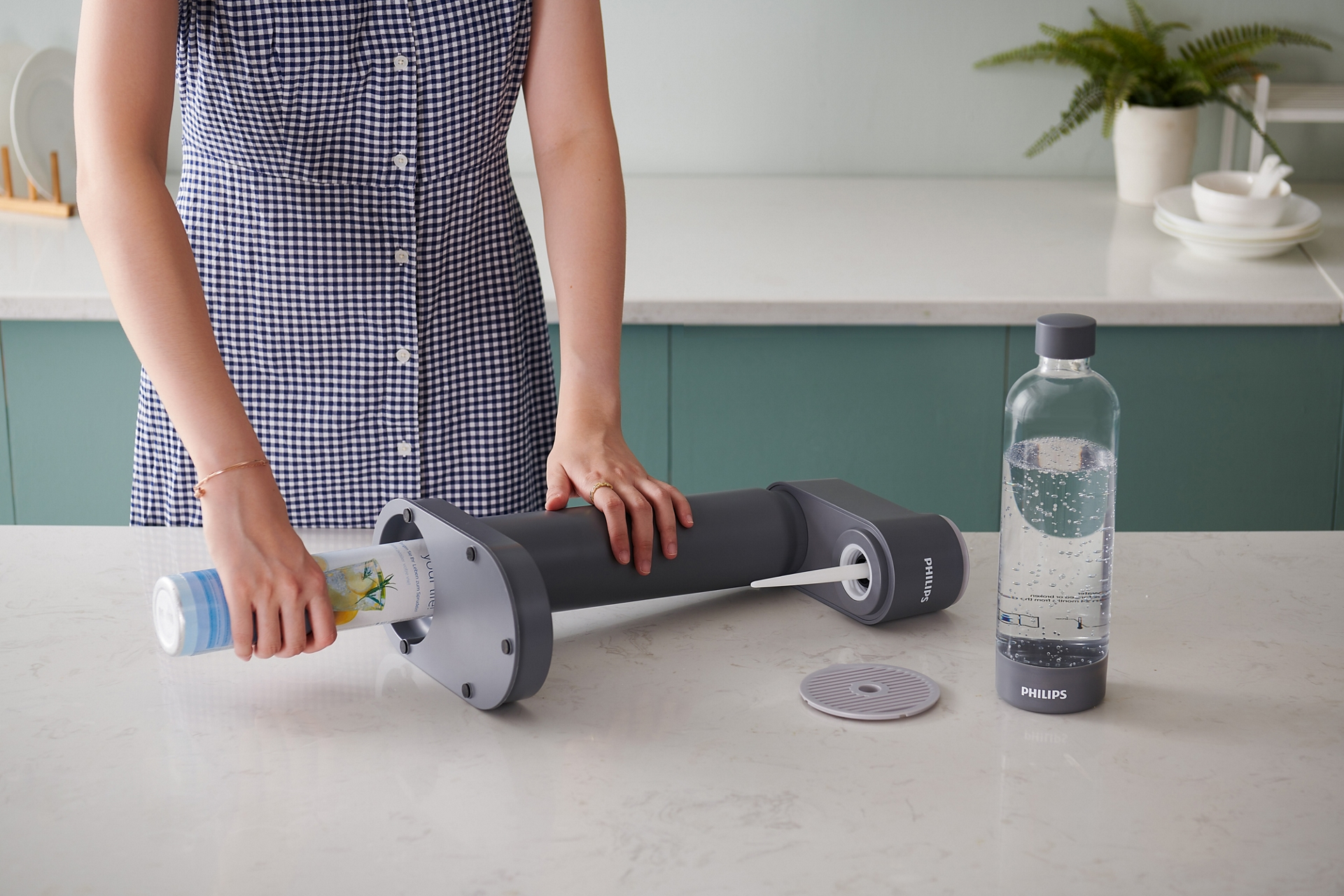 Una donna inserisce un filtro in una macchina per l'acqua grigia, una bottiglia d'acqua è a destra. Lo sfondo è una cucina.