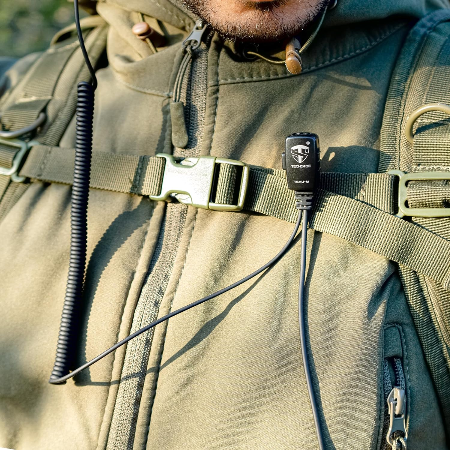 Una persona indossa una giacca e uno zaino verdi con un microfono. Il microfono è etichettato 'TECHSIDE TSAU-M'.