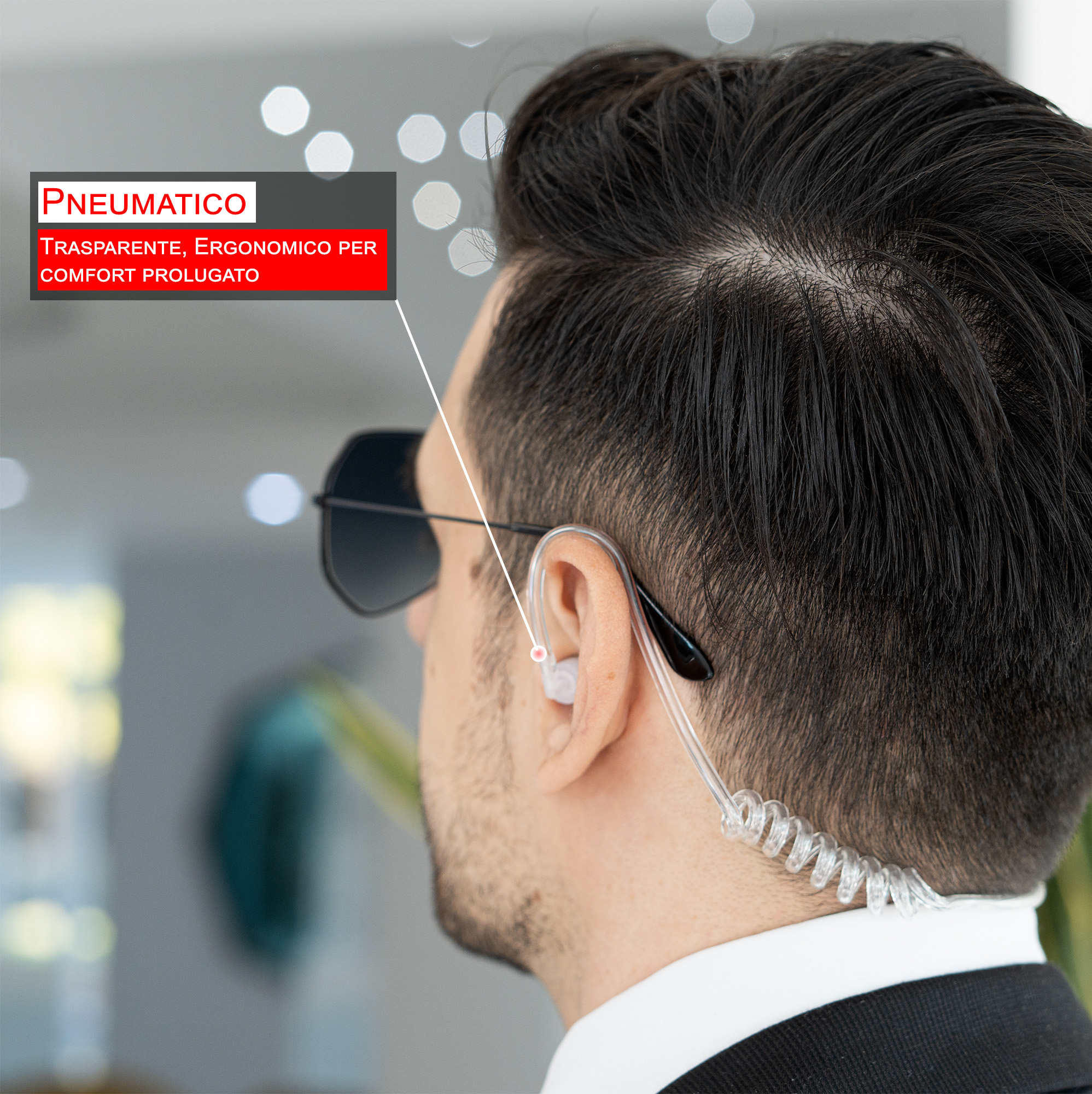 Un uomo con occhiali da sole e auricolare. Sovrapposizione di testo: Pneumatico, Trasparente, Ergonomico per Comfort Prolungato.