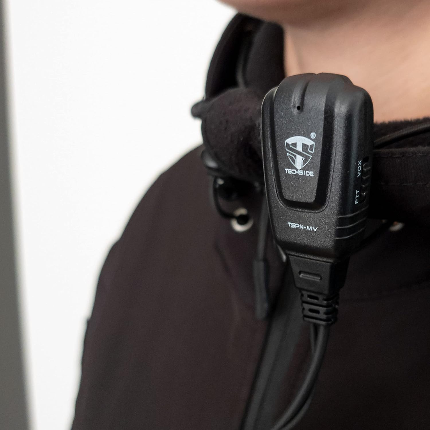 Un microfono Techside nero è agganciato alla giacca nera di una persona. Il microfono ha un logo e la scritta 'TSPN-MV'.