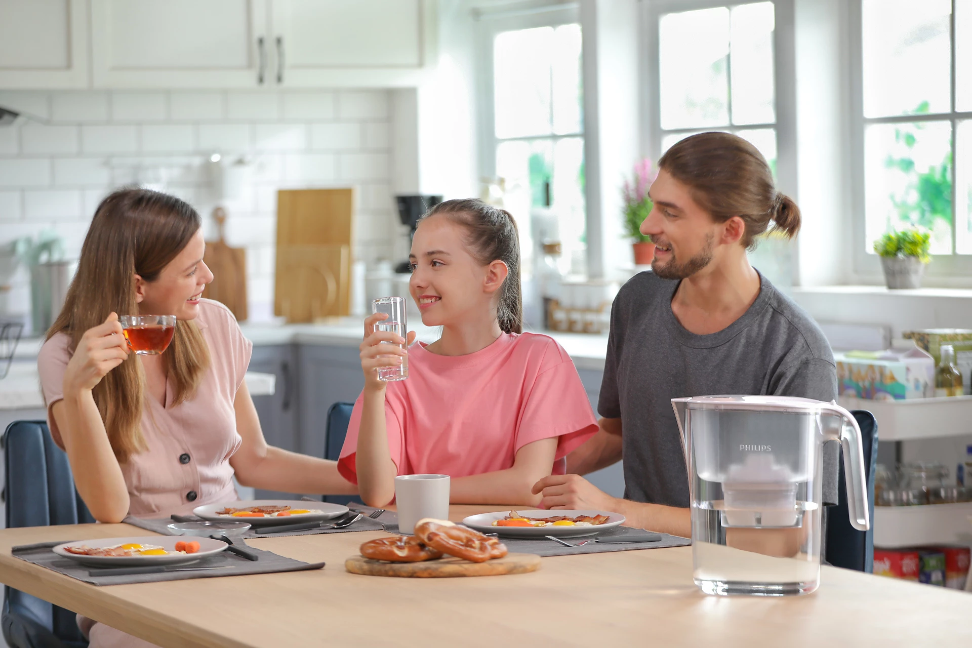 Famiglia che fa colazione. La donna beve tè. Ragazza e uomo bevono acqua. Tavolo con cibo e filtro dell'acqua.