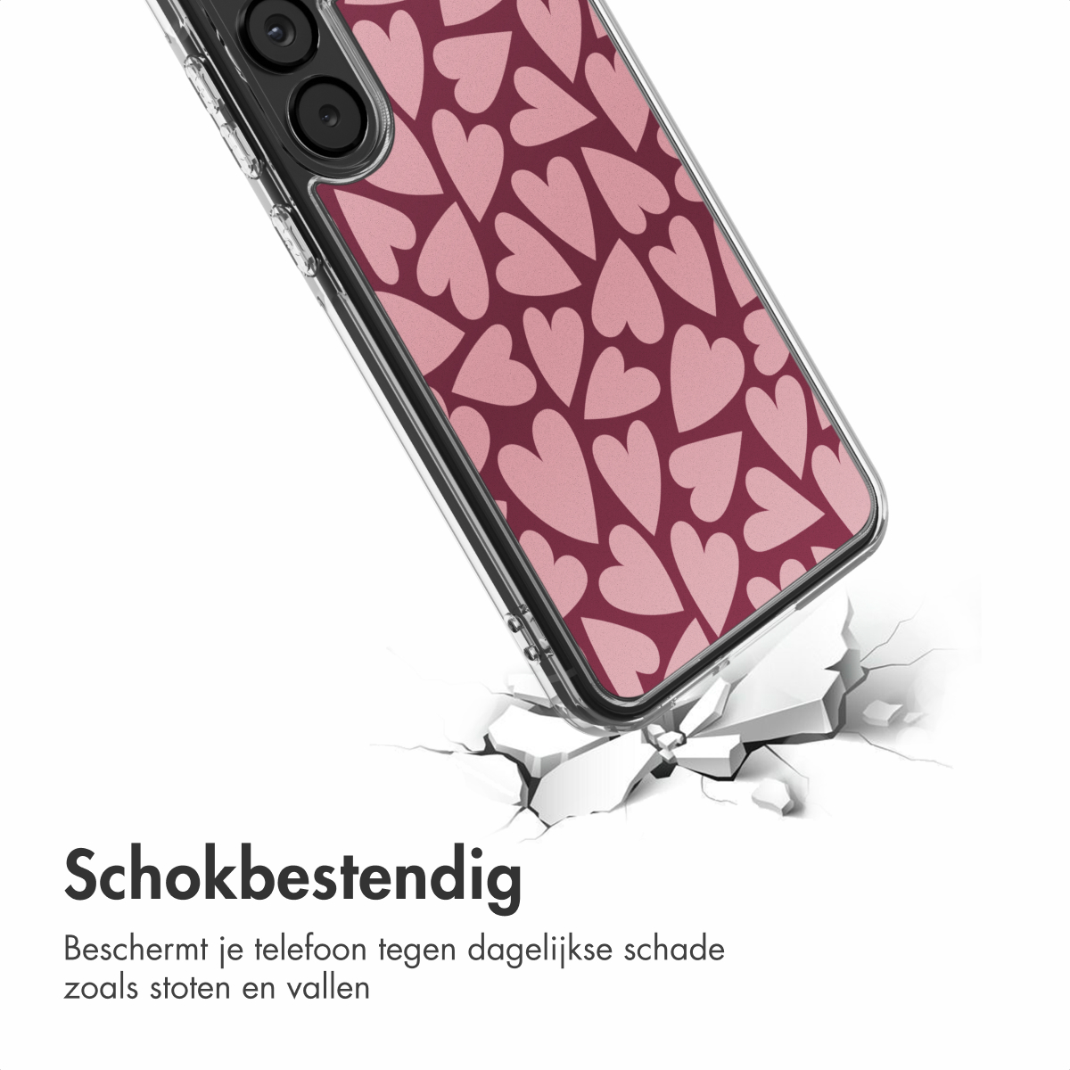 Een telefoonhoesje met roze hartjes op een bordeauxrode achtergrond breekt een oppervlak. Scheuren verspreiden zich van de impact. De telefoon staat schuin.
