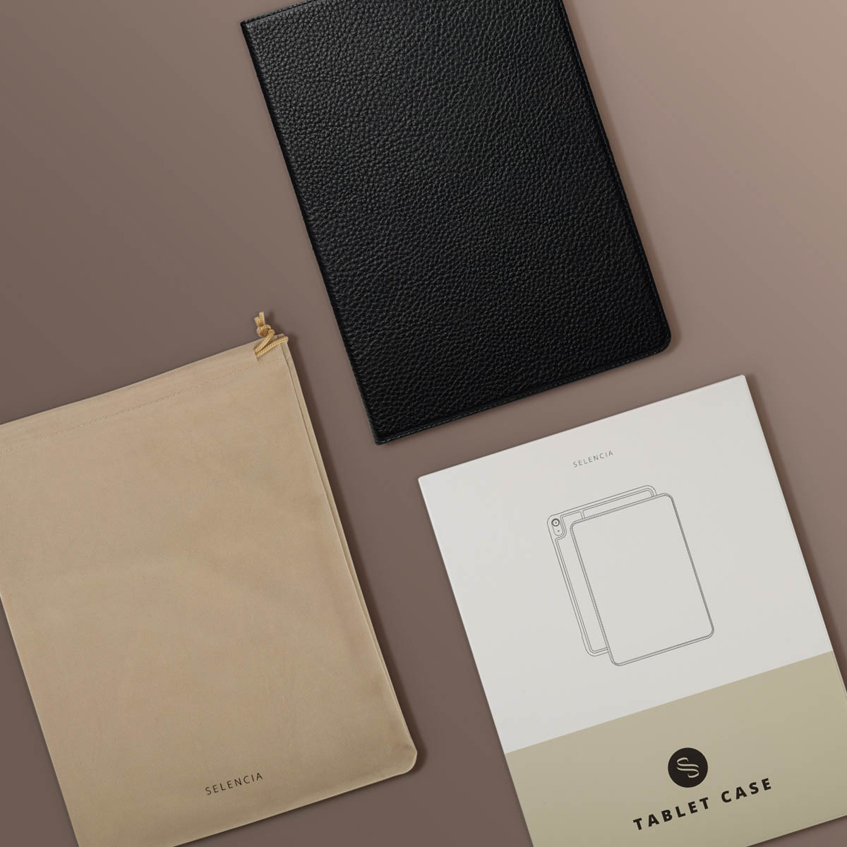 Black leather tablet case, beige pouch, and product brochure on a brown surface. The brochure says 'Tablet Case'.