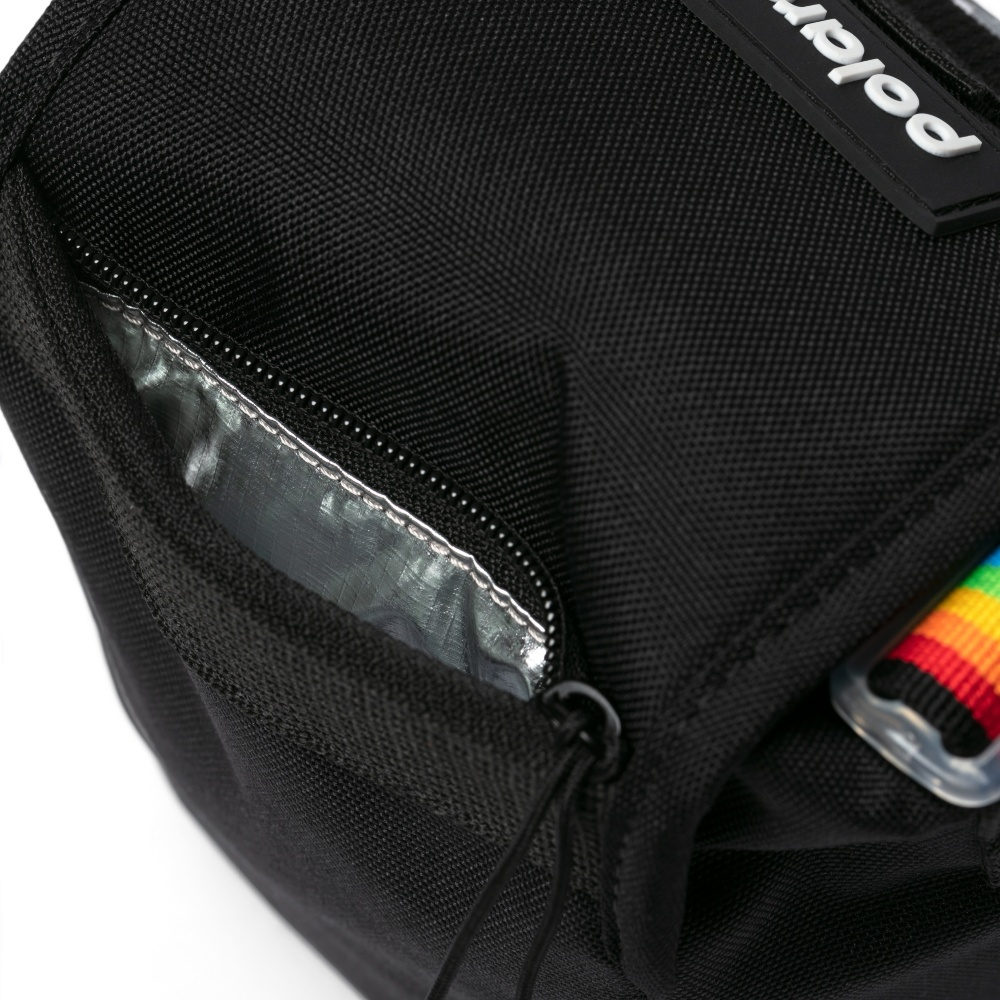 Nahaufnahme einer schwarzen Tasche mit silbernem Innenfach. Regenbogenriemen und das Wort 'polar' sind sichtbar. Die Tasche liegt auf weißem Grund.