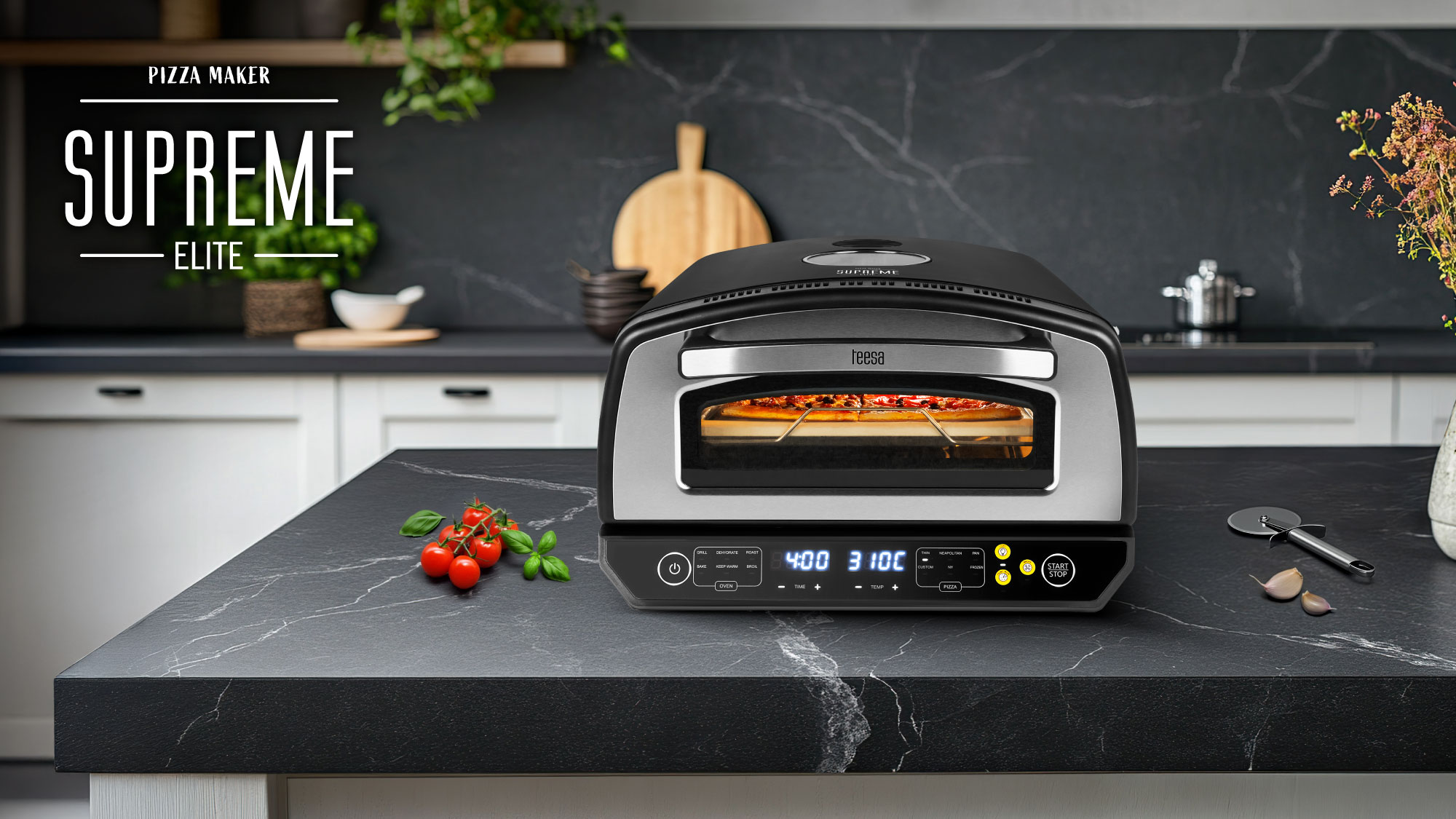 Pizzamaker 'Supreme Elite' stoi na czarnym blacie. W piekarniku jest pizza. Pomidory i bazylia na pierwszym planie.