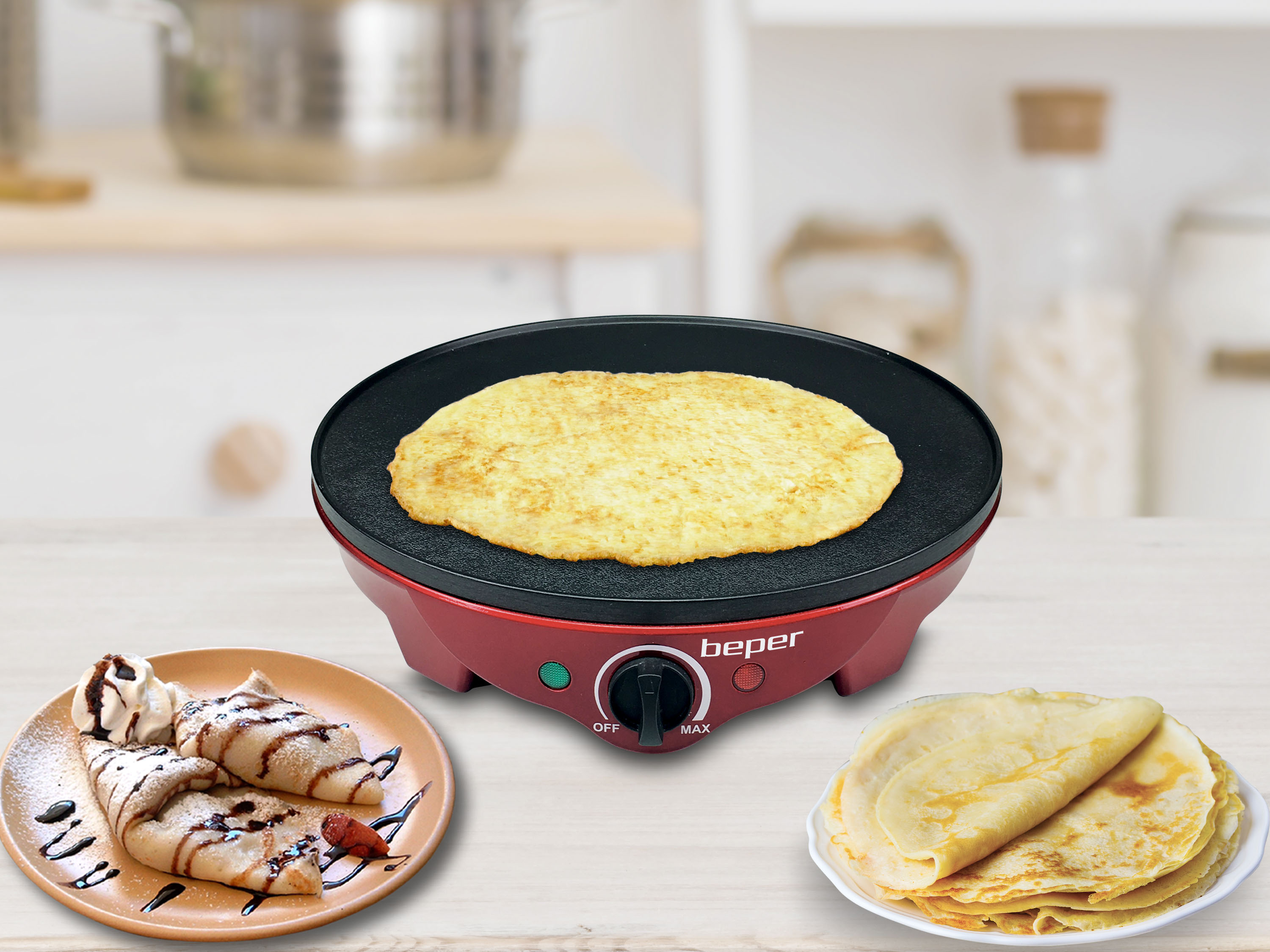 Ein roter Crêpes-Maker mit einem Crêpe darauf und zwei Teller mit Crêpes auf einem Holztisch.