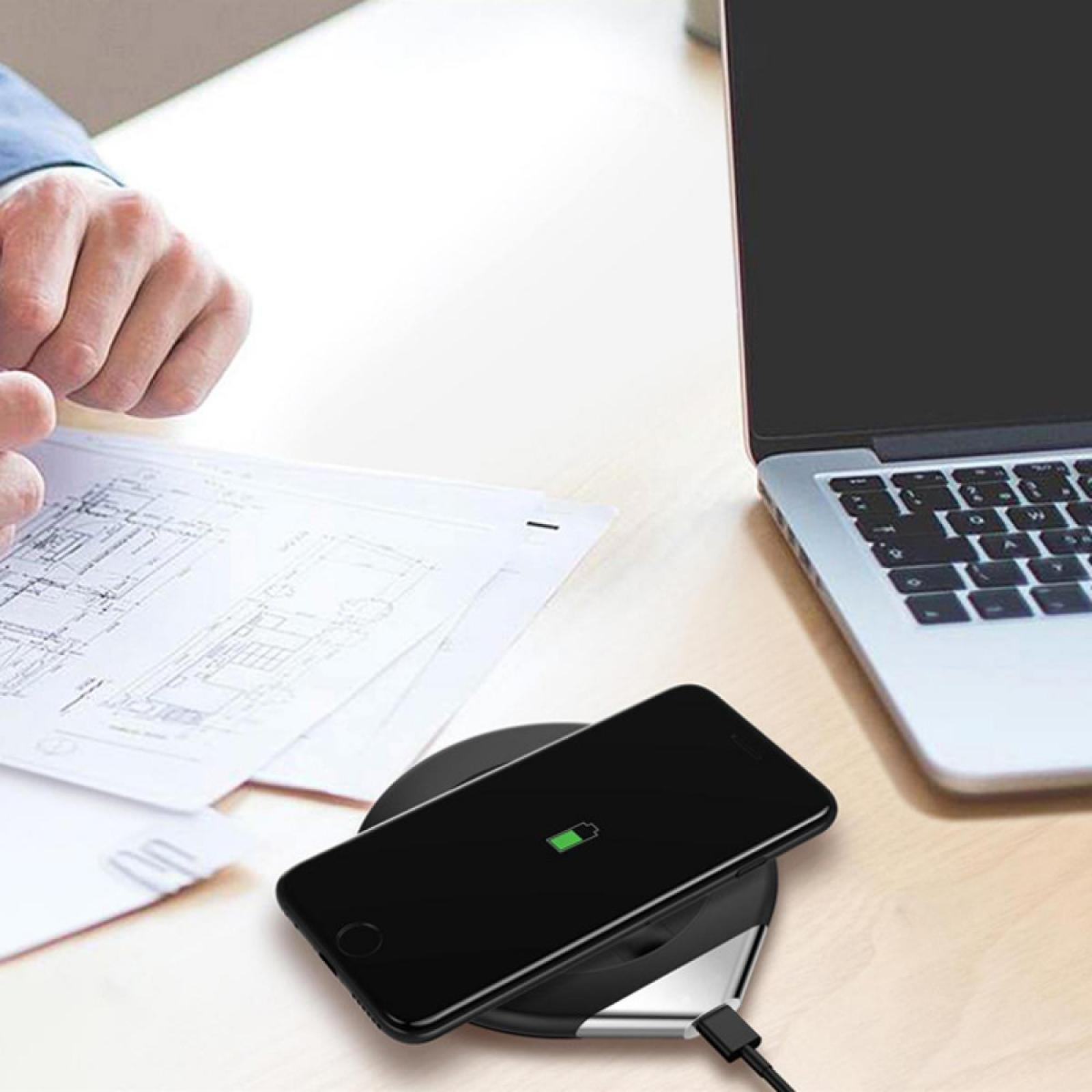 Ein schwarzes Telefon auf einem kabellosen Ladegerät, ein Laptop und Blaupausen auf einem Tisch.