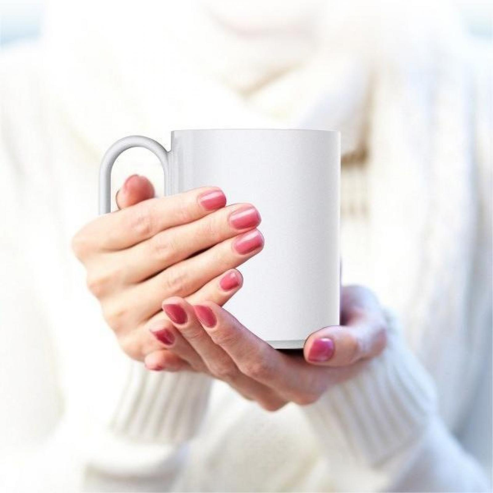 Hände halten einen weißen Becher mit pinkfarbenem Nagellack. Die Person trägt einen weißen Pullover. Fokus auf den Becher und die Hände.
