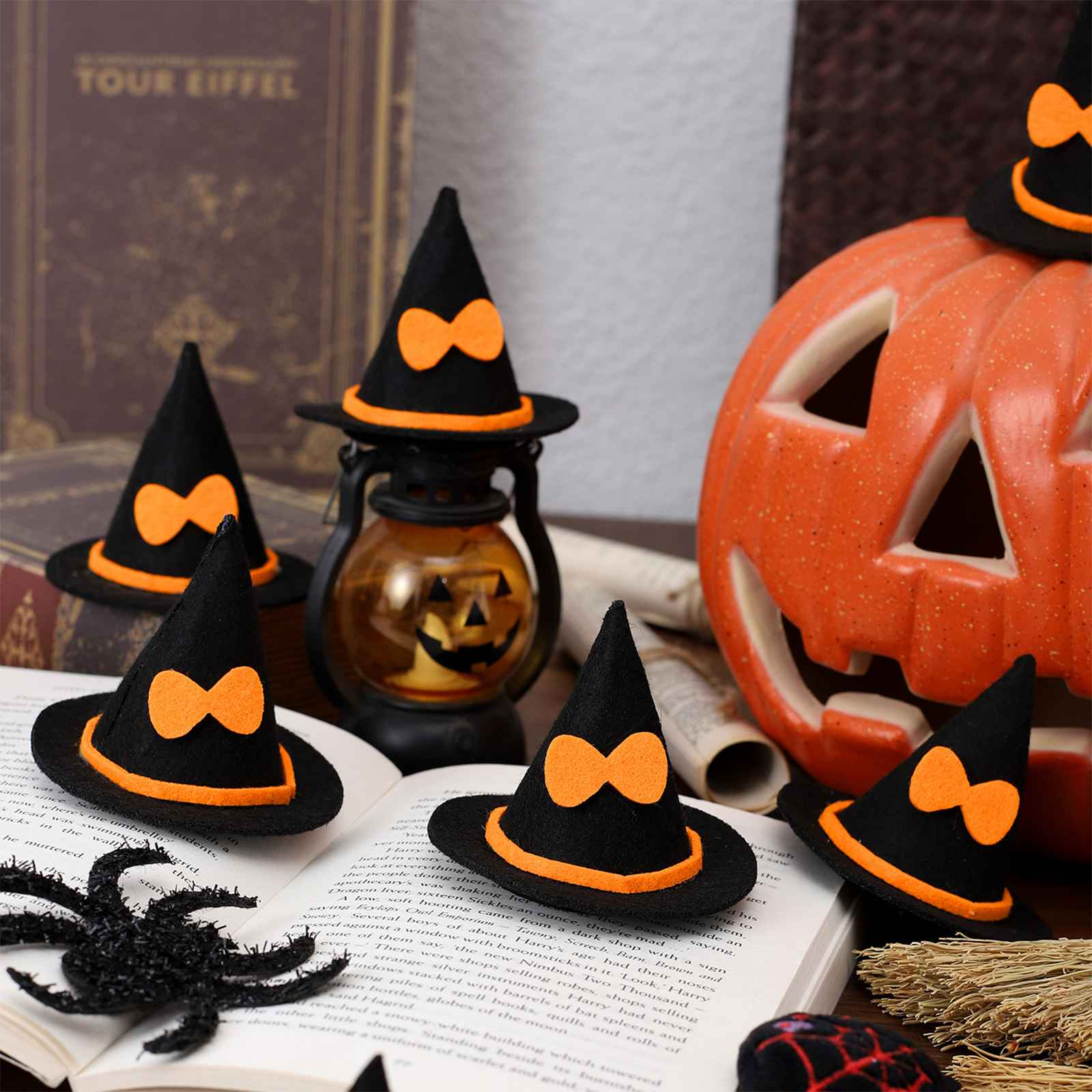 Halloween-Szene: Schwarze Hexenhüte mit orangefarbenen Schleifen, ein geschnitzter Kürbis, eine Spinne und eine Laterne.