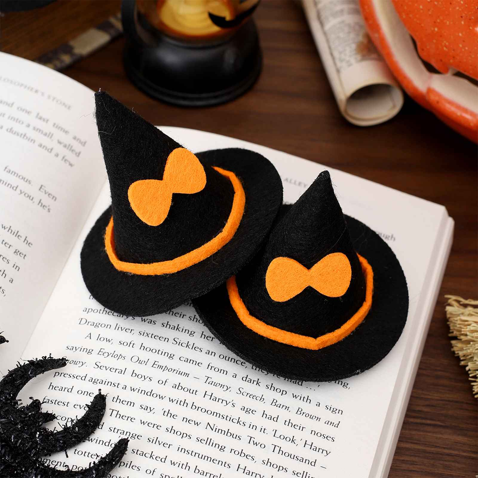 Zwei schwarze Hexenhüte mit orangefarbenen Schleifen und Verzierungen liegen auf einem Buch. Eine schwarze Spinne und andere Halloween-Dekorationen sind vorhanden.