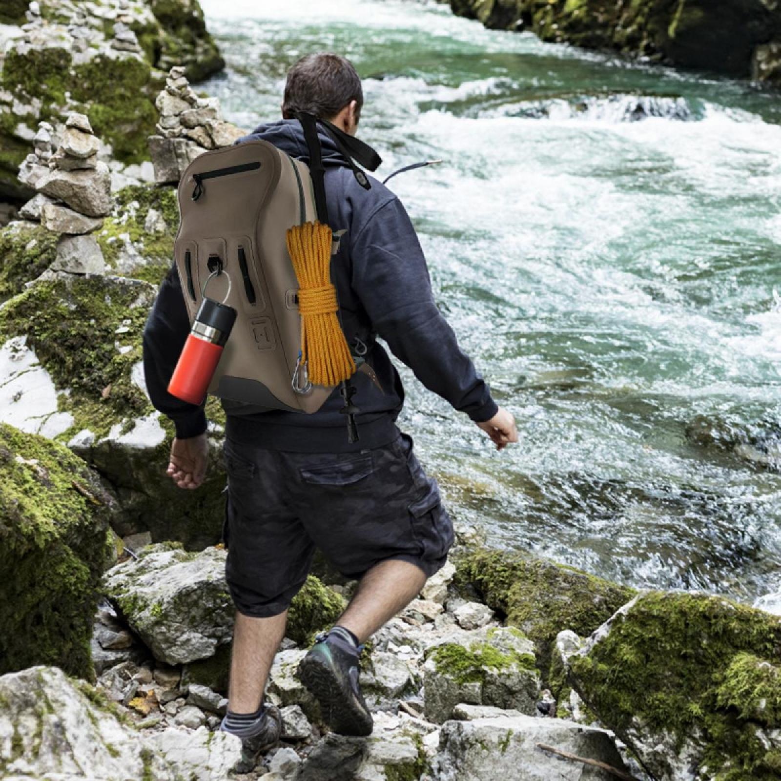 Ein Mann wandert am Fluss. Er trägt einen Rucksack mit Seil und Wasserflasche. Felsen und grünes Moos umgeben ihn.