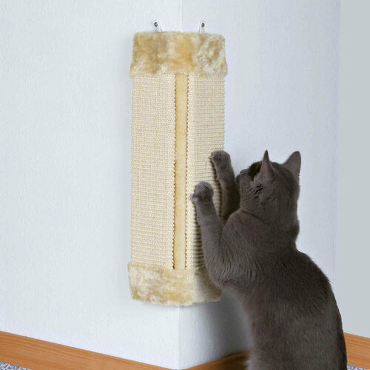Un gato gris rasca un rascador de color canela fijado a una pared en esquina. El poste es de material tejido y está adornado con piel sintética.
