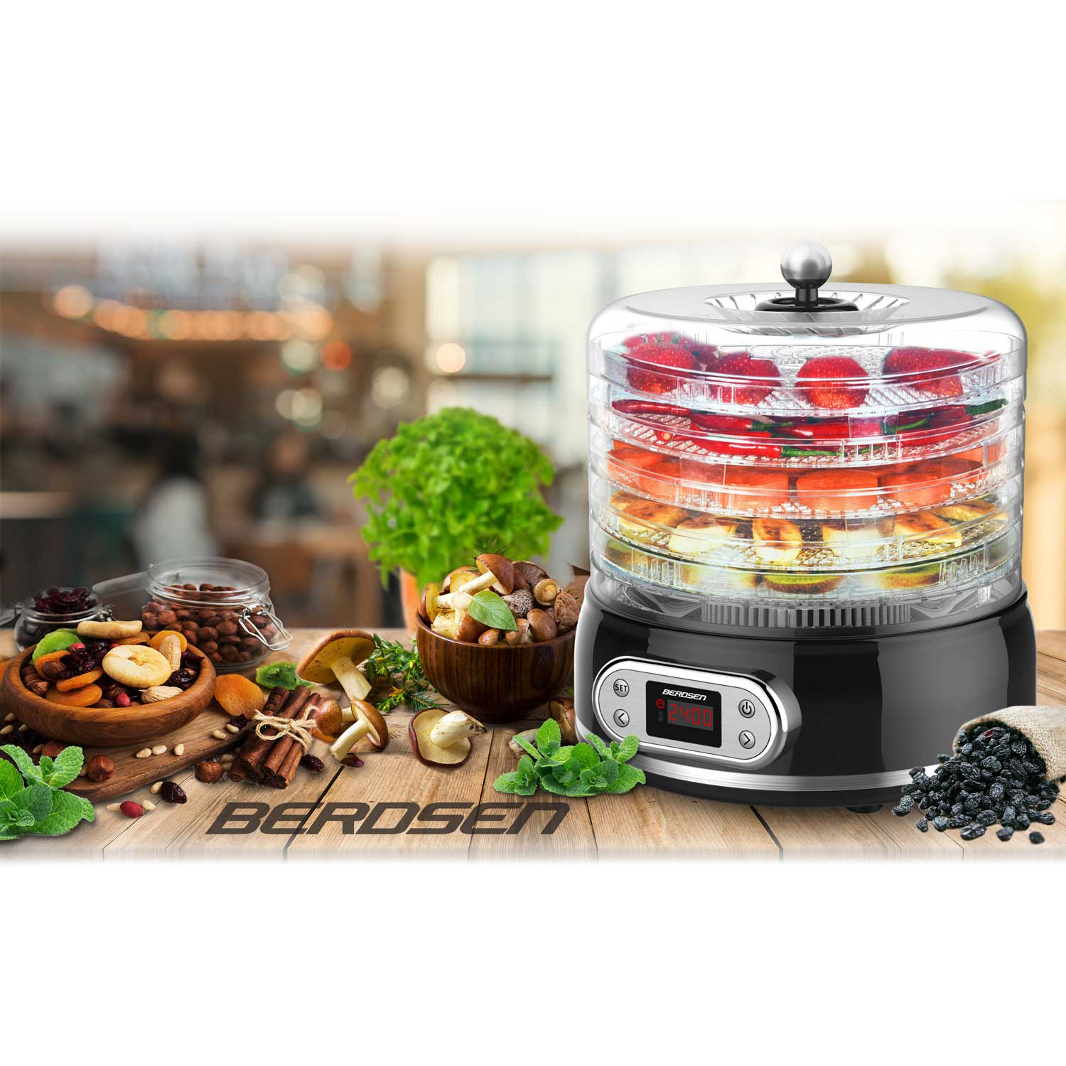 Suszarka do żywności z przezroczystymi tackami wypełnionymi owocami. Różne suszone produkty i świeże zioła otaczają ją na drewnianym stole.