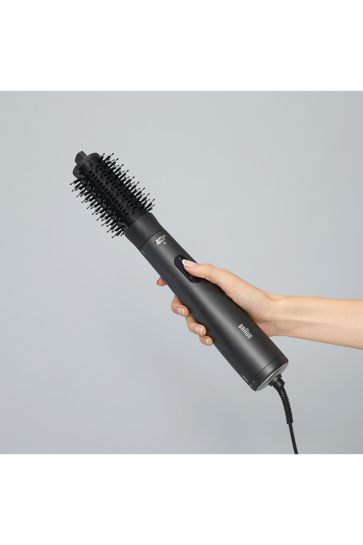 Una mano che tiene un arricciacapelli nero Braun. L'arricciacapelli è collegato. Lo sfondo è grigio.