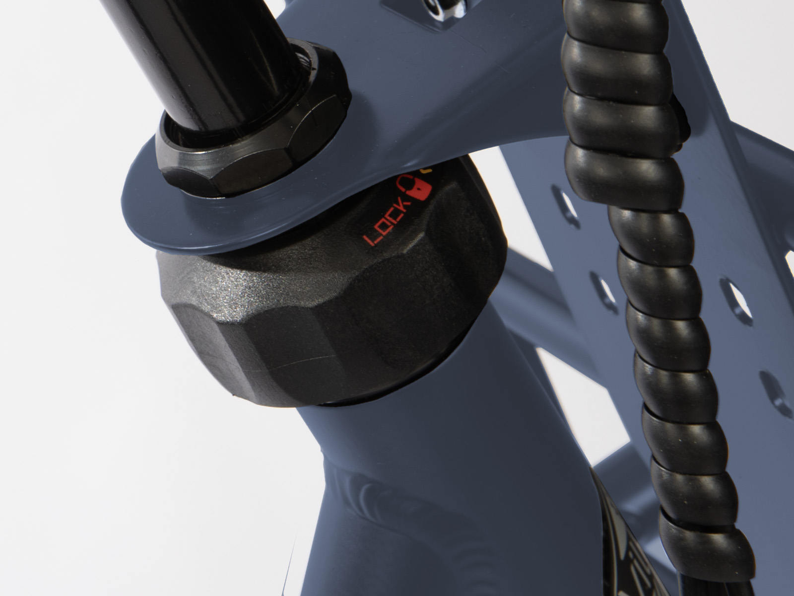 Close-up van een fietsonderdeel. Een zwart zeshoekig slot is zichtbaar, met "LOCK" in rood. Een opgerolde zwarte kabel loopt ernaast.