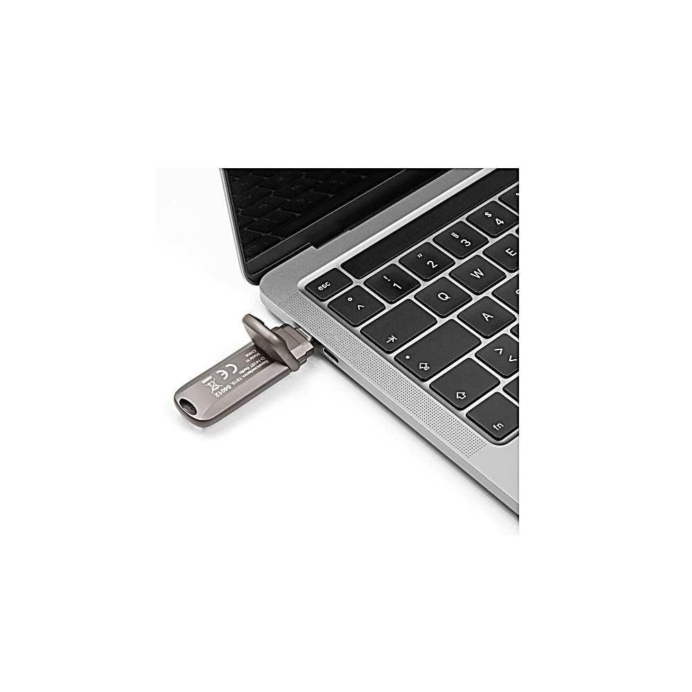 Un'unità USB grigia è collegata a un laptop argentato. La tastiera del laptop è visibile, insieme allo schermo e a uno sfondo bianco.