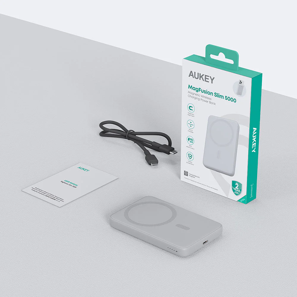 Banco de energía AUKEY MagFusion Slim 5000, caja y accesorios sobre una superficie blanca. El banco es gris.
