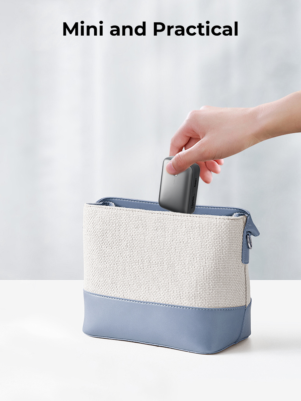 Una mano mette un piccolo dispositivo grigio in una borsa blu e bianca. Il testo 'Mini and Practical' è in alto.