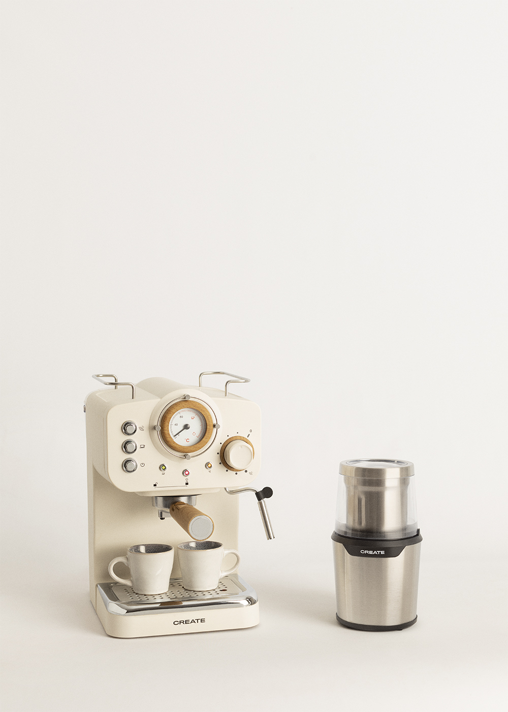 Máquina de espresso beige con dos tazas y un molinillo de café plateado sobre fondo blanco.