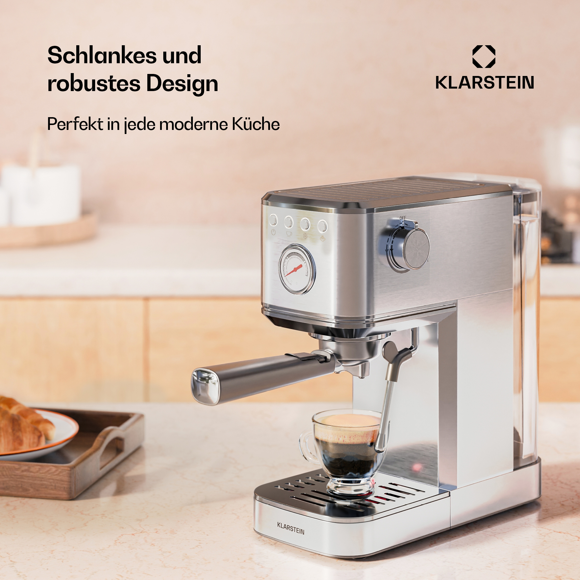 Una cafetera espresso plateada con una taza de café. Una bandeja con croissant en el fondo.