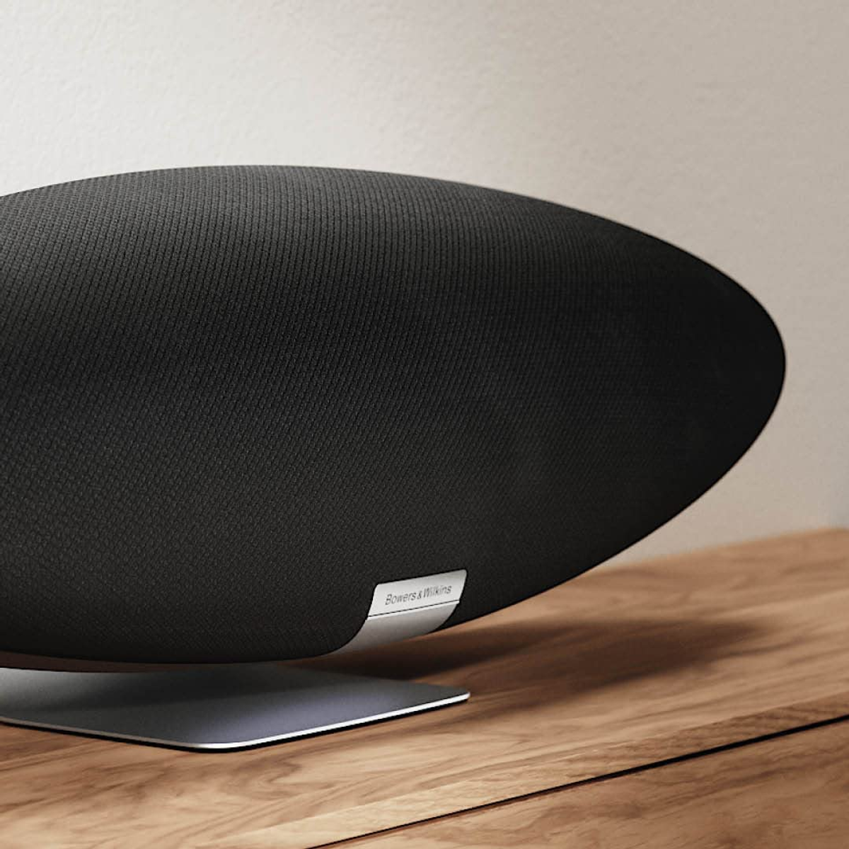 Ein schwarzer ovaler Lautsprecher mit Metallfuß steht auf einer Holzoberfläche. Der Lautsprecher hat ein Bowers & Wilkins Logo.