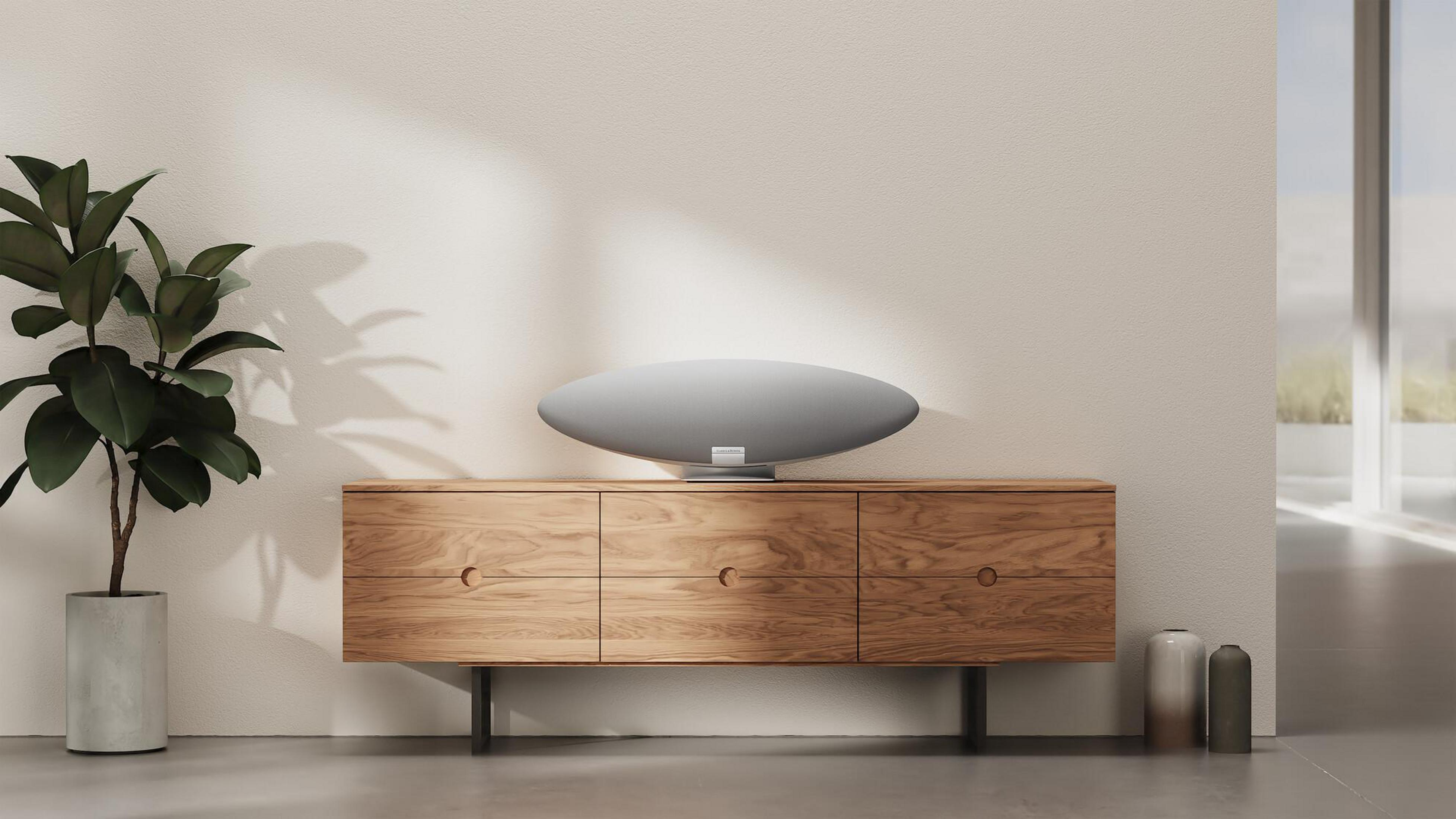 Ein modernes Wohnzimmer mit Holzschrank, grauem Lautsprecher, Pflanze und zwei Vasen. Helles Licht kommt vom Fenster.