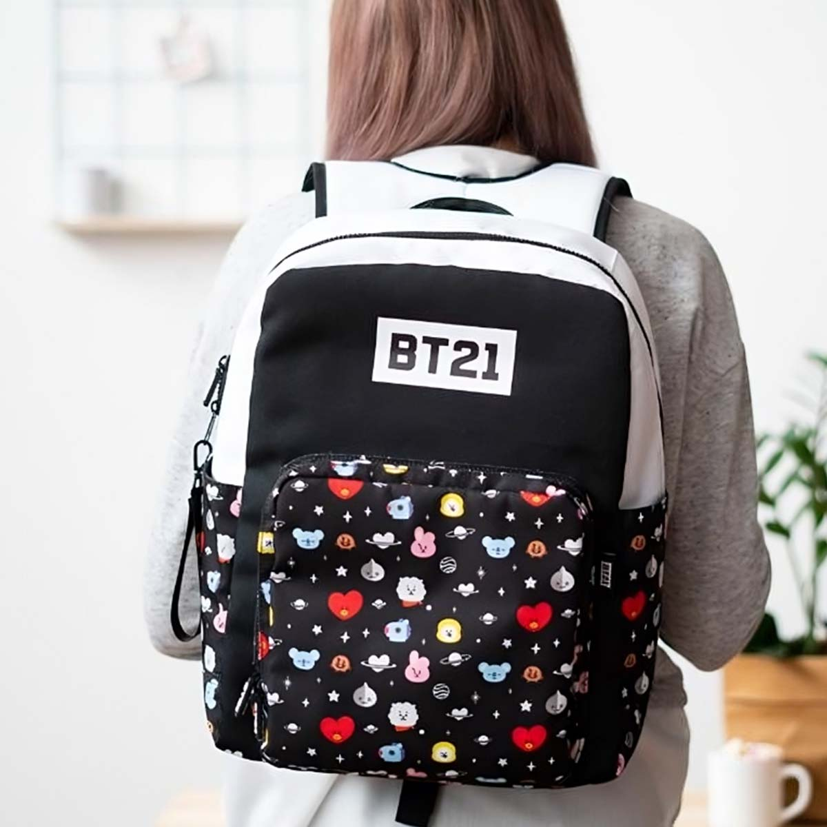 Una persona indossa uno zaino nero con logo BT21 e personaggi colorati. Lo zaino ha dettagli bianchi e neri.