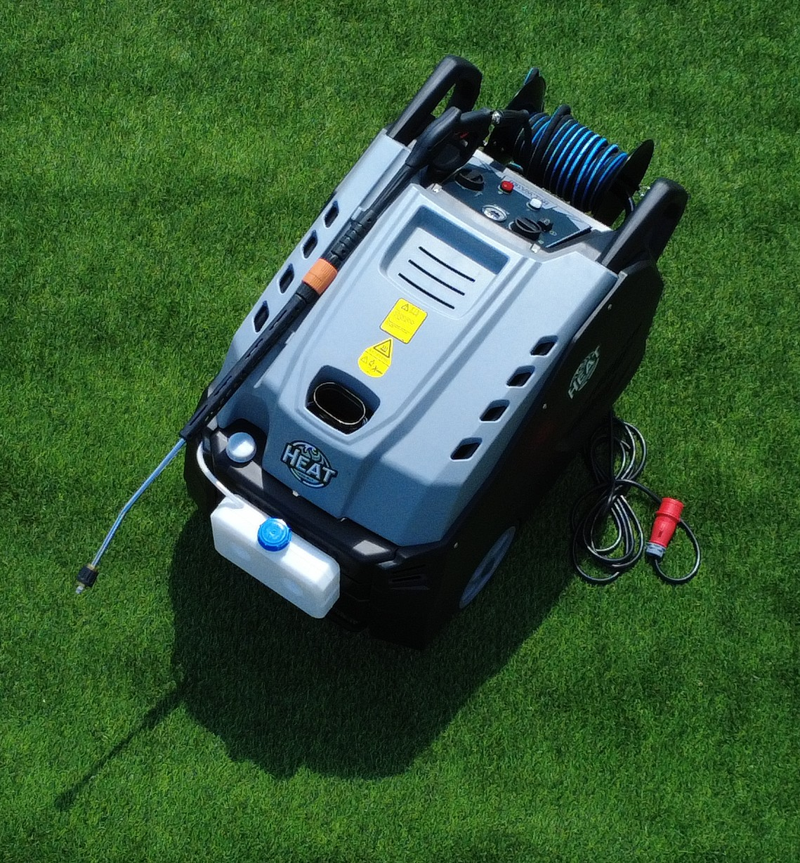 Ein grau-schwarzer Hochdruckreiniger auf grünem Gras. Er hat eine blaue Schlauchtrommel, eine Düse und einen weißen Wassertank.