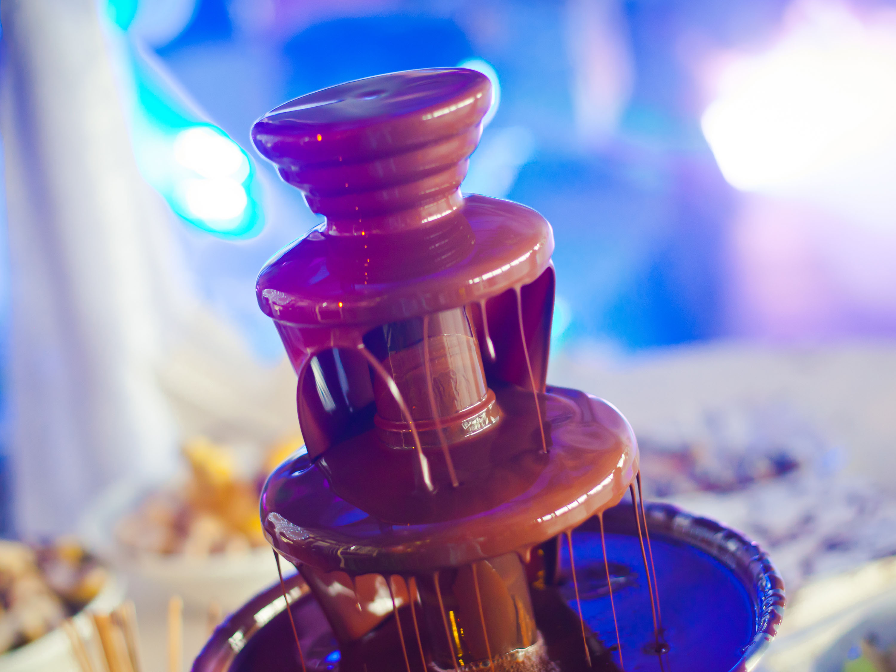 Una fontana di cioccolato con cioccolato fondente a cascata. Lo sfondo ha luci blu e bianche.