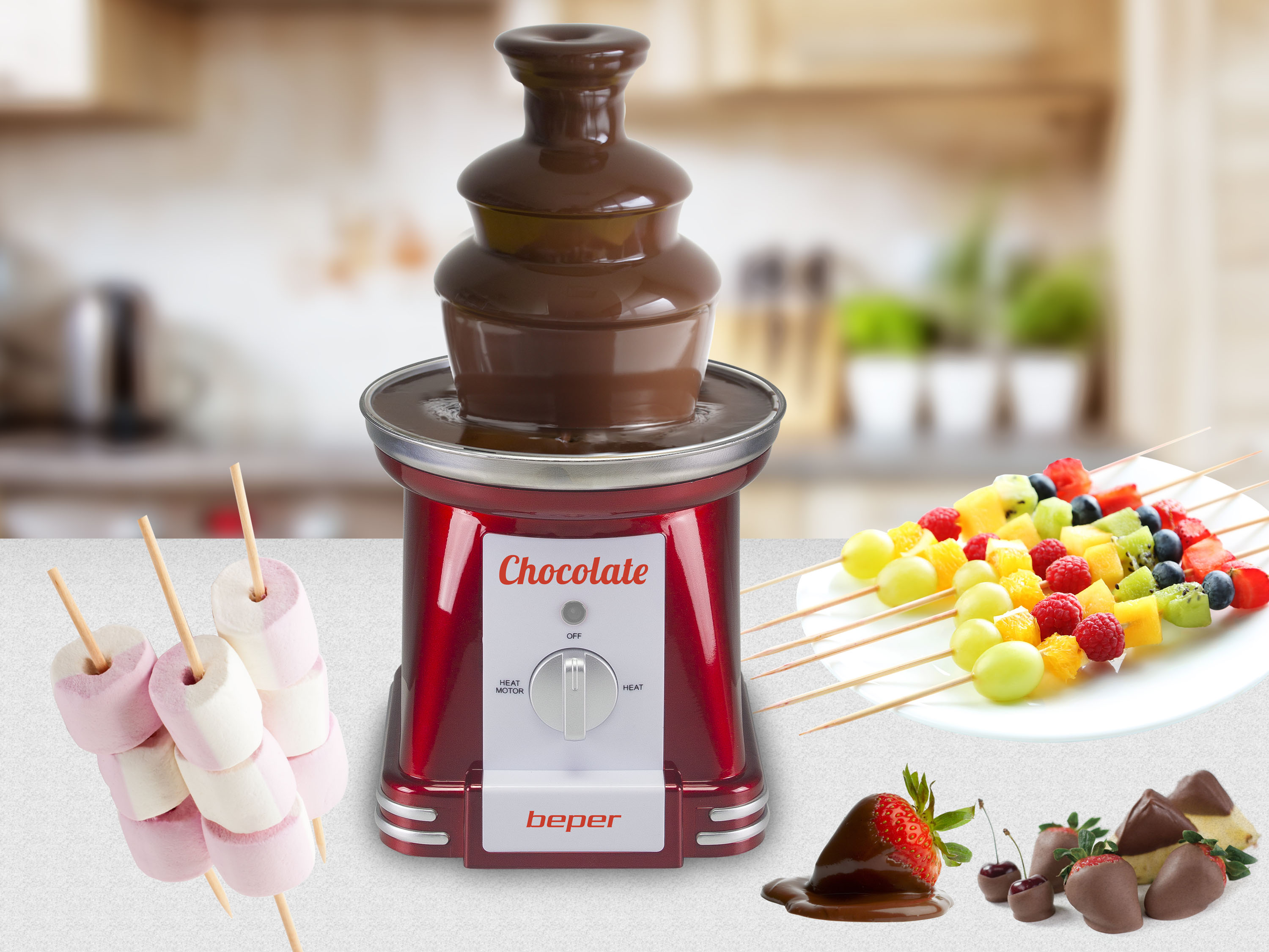 Una fontana di cioccolato con spiedini di frutta, fragole ricoperte di cioccolato e marshmallow. Una cucina sullo sfondo.