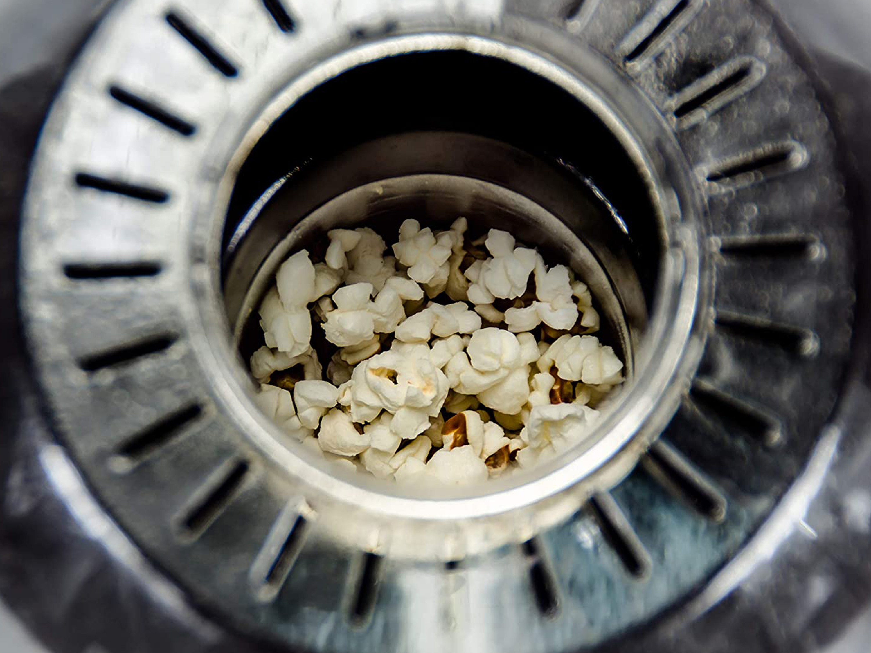 Primo piano di popcorn in un colino di metallo. Popcorn bianco riempie il contenitore interno. Il colino ha delle fessure.