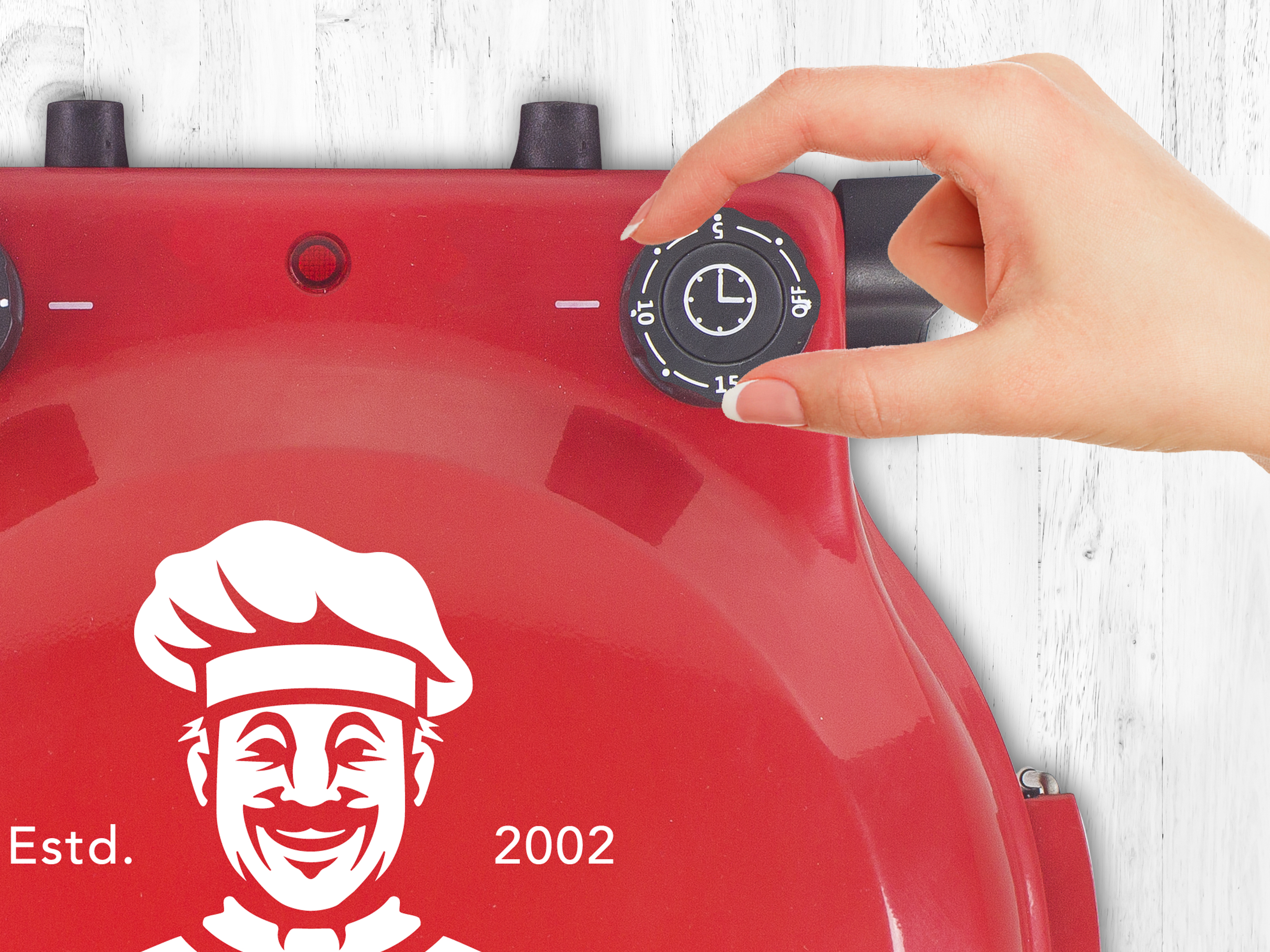 Un elettrodomestico rosso con una mano che gira il timer. L'apparecchio ha un logo dello chef.