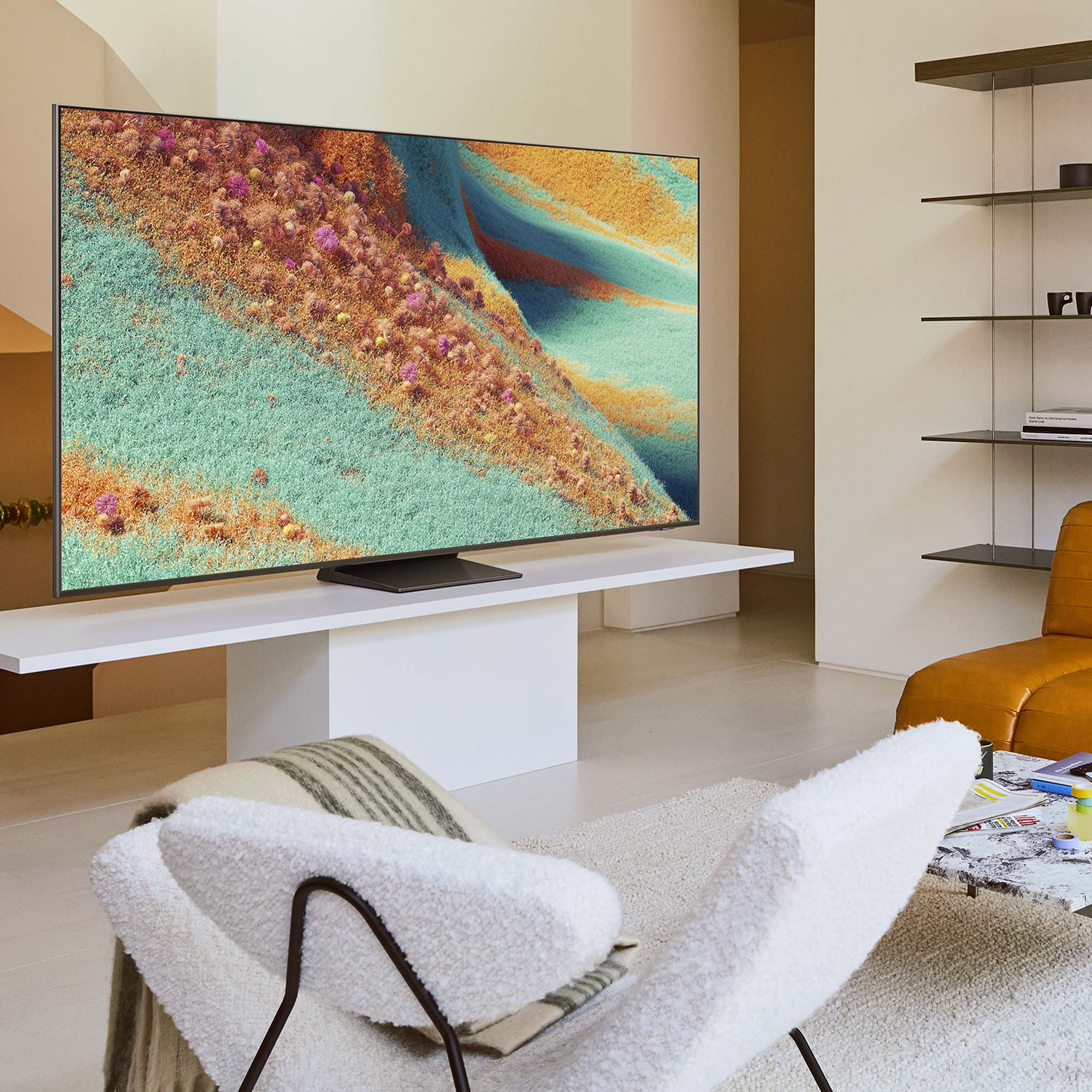 Soggiorno con una grande TV che mostra un paesaggio astratto. Una sedia bianca, un tappeto e un divano sono in primo piano.